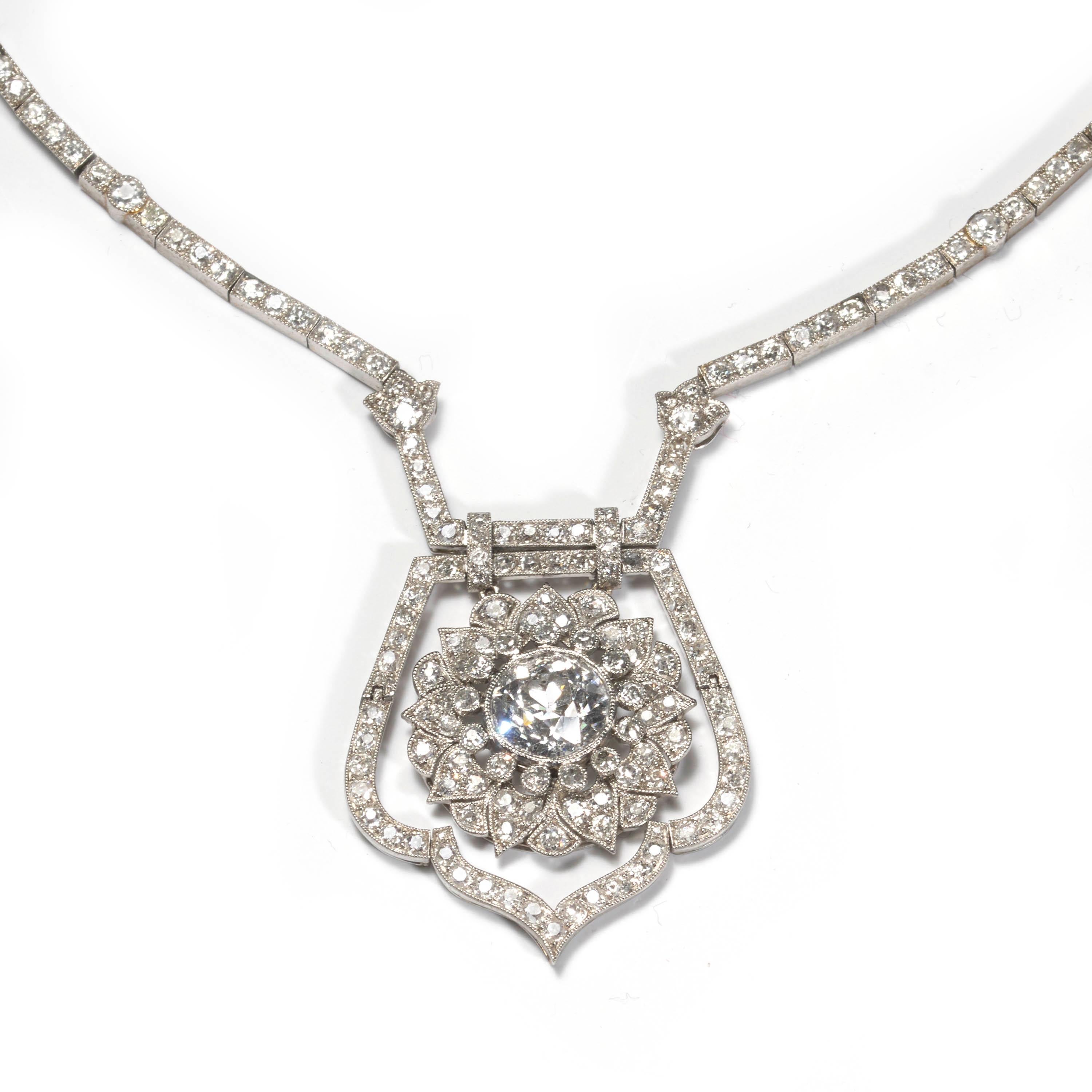 An Art Deco diamond necklace, designed as an old-cut diamond weighing an estimated 3.75ct, set in the centre of a floral cluster motif and suspended within an articulated old-cut diamond surround, further suspended from an integrated pavé set