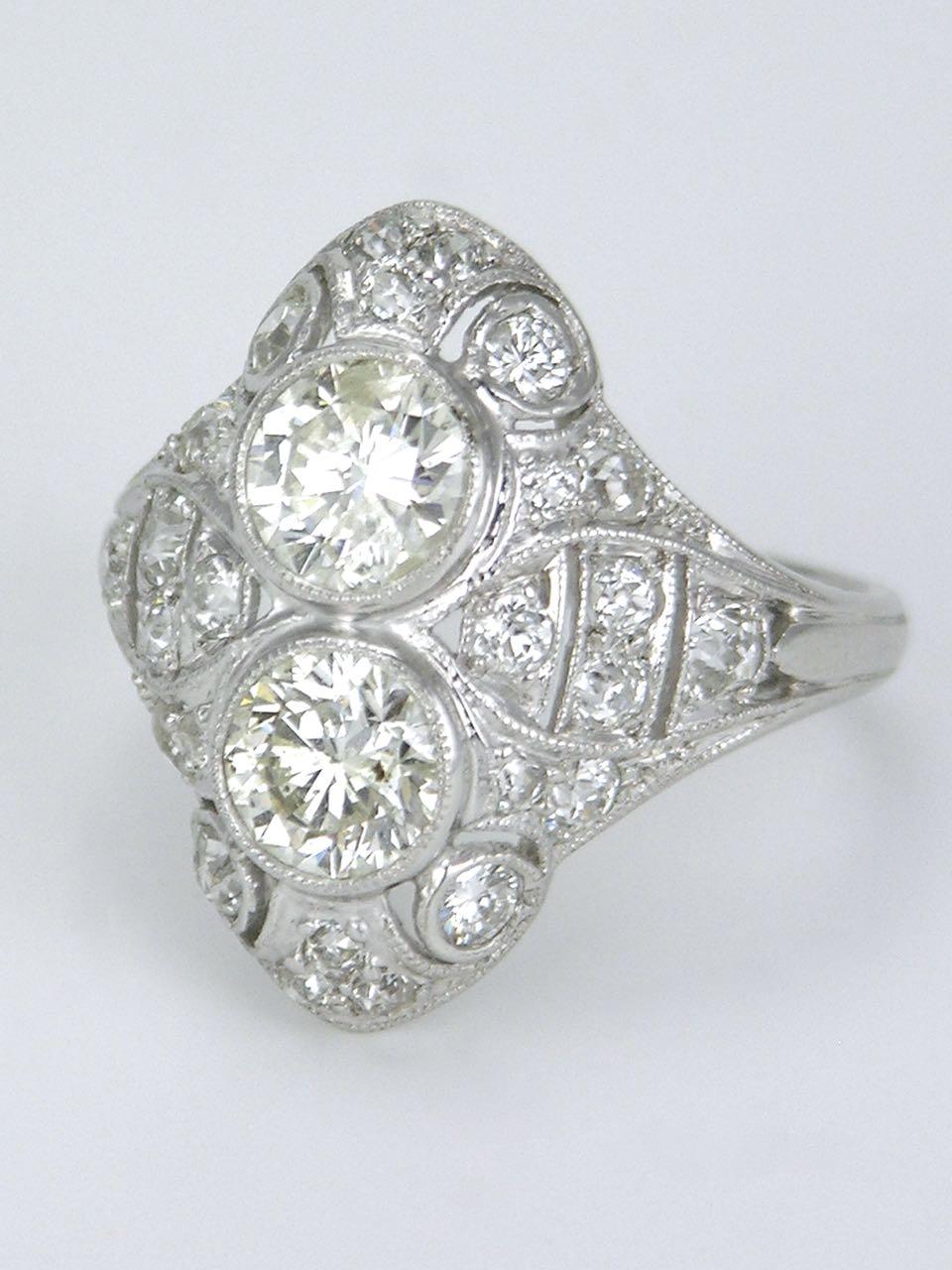 A stunning Art Deco diamond and platinum two stone ring consisting of a pair of brilliant cut diamonds bezel set and surrounded by 24 old cut diamonds in a fretted plaque setting.  This is a truely beautiful design that sits low on the hand and