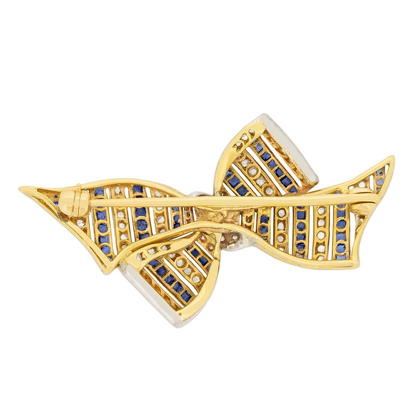 This intricate art deco brooch laces together sapphires and diamonds to form a sweet bow. Alternating stripes of blue sapphires and diamonds make a pretty pattern. The french cut sapphires total to 0.65 carat, while the rose cut diamonds total to