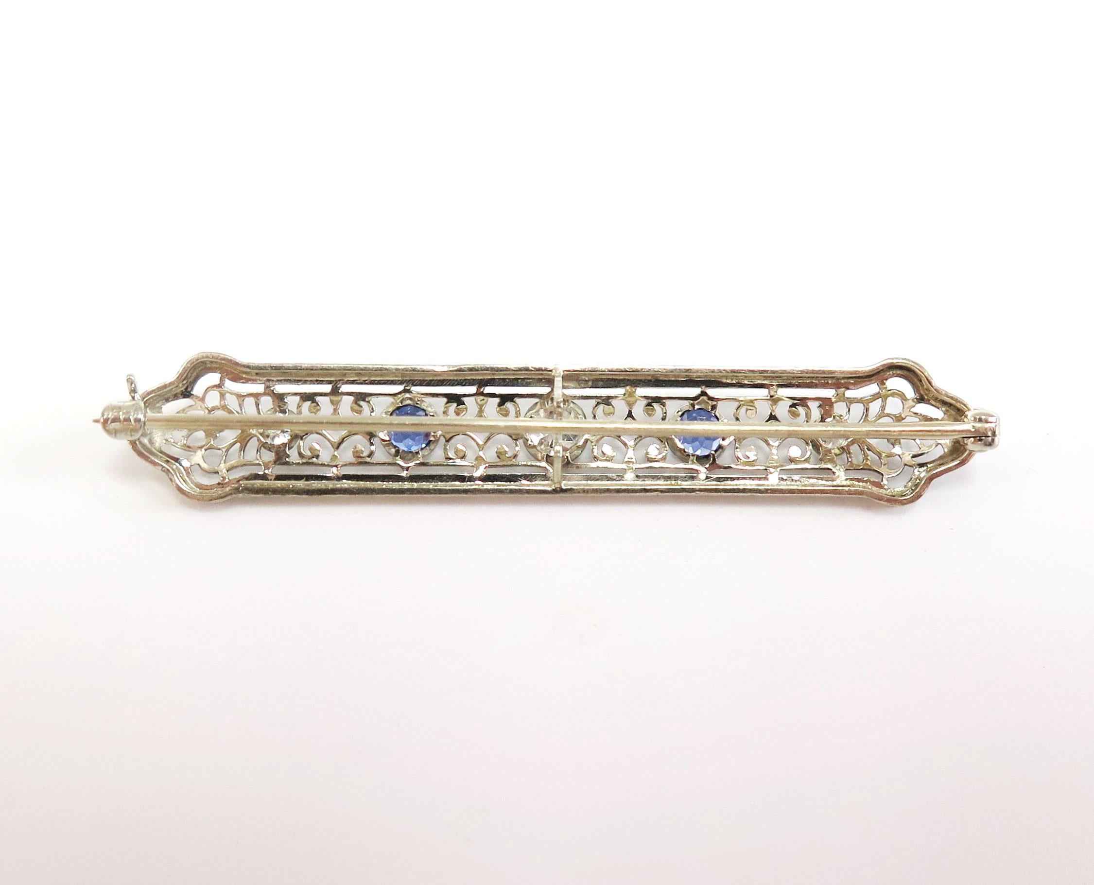 One bright white 0.20 Carat Old Mine Cut Diamond sparkles from the center of this delicate filigree bar pin. On either side is a deep sea Blue Sapphire and two white Old European Cut Diamonds. 

The total weight of the three Diamonds is 0.28 Carats,