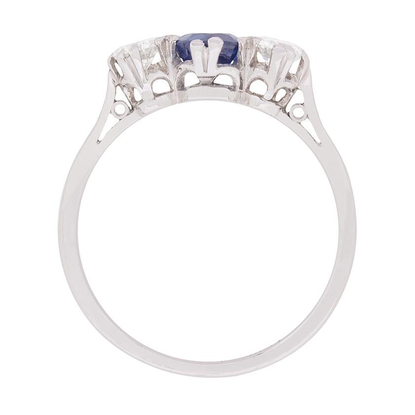 A beautiful little three stone engagement ring featuring a deep blue sapphire in the centre. It wonderful gemstone weighs 0.65 carat and is a natural stone. It has been claw set and is highlighted by the two adjacent diamonds, also claw set. The