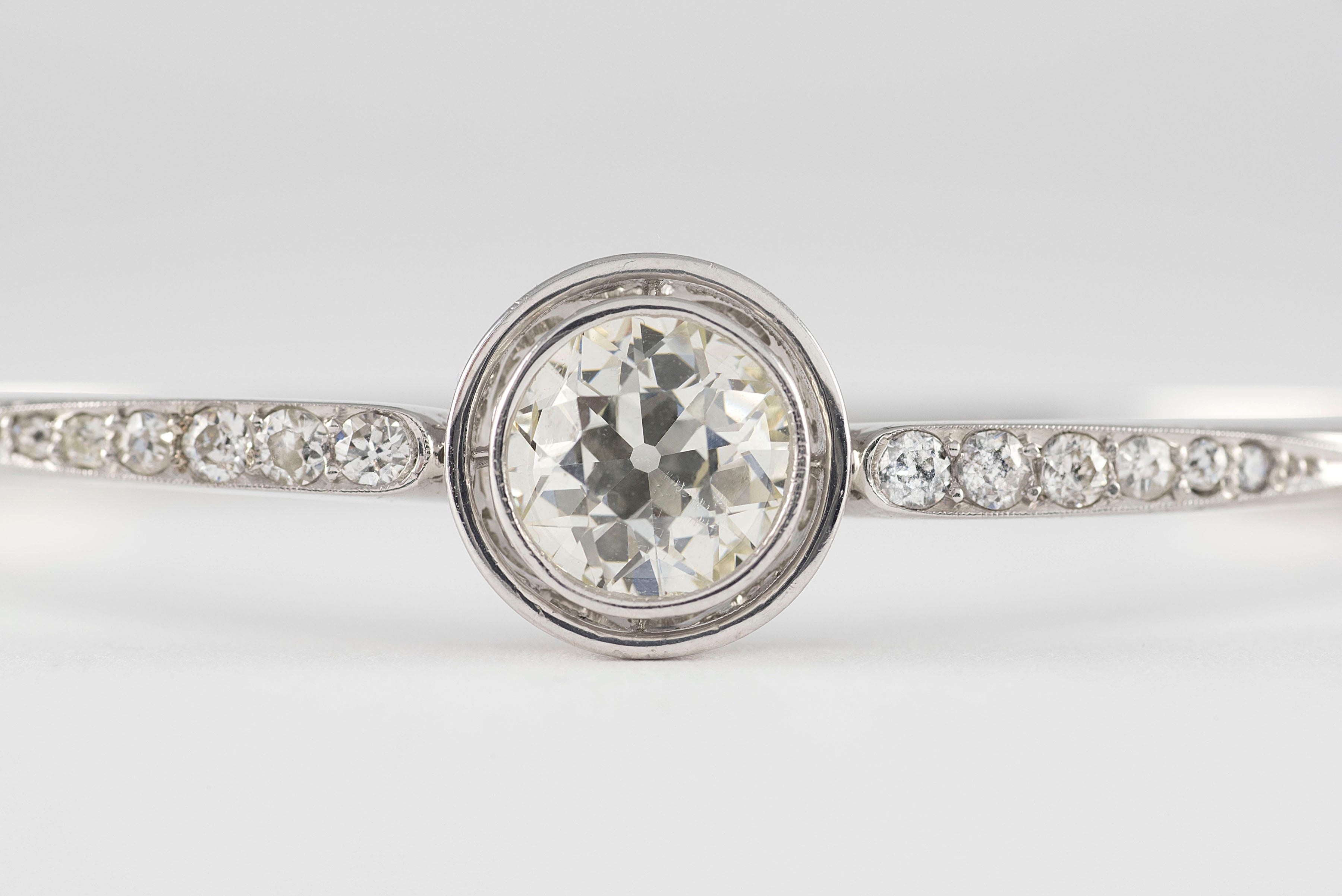 An Old European cut diamond totaling approximately 2.32 carats, K color, SI1 clarity bezel set centers this antique Art Deco bangle bracelet flanked by twelve Old Mine cut diamonds totaling approximately 0.50 carats and handcrafted in 18kt white
