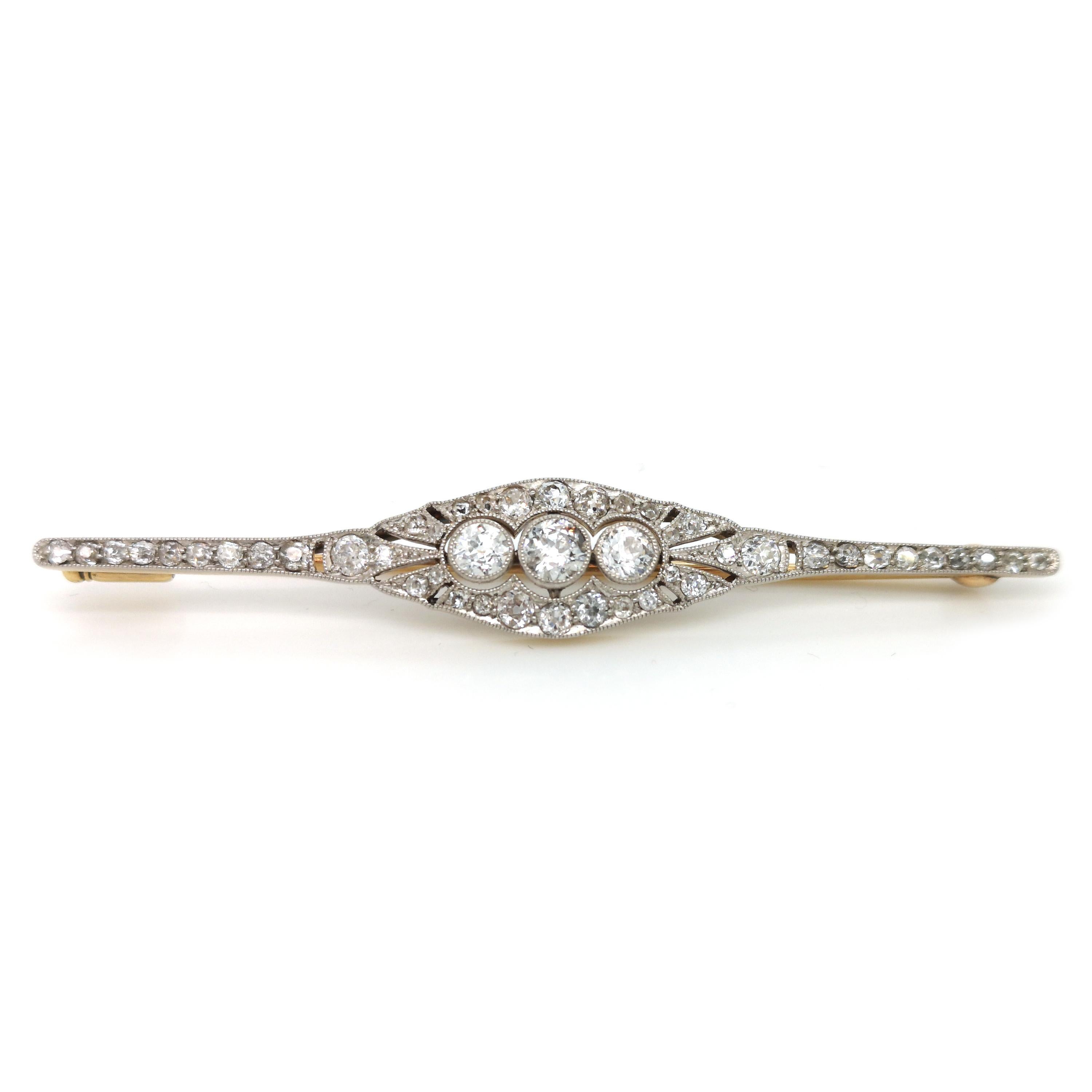 An Art Deco diamond bar brooch, set with old-cut diamonds, with three larger centre stones, in millegrain edged rub over settings, surrounded by grain set old-cut diamonds, in a millegrain edged open framework Art Deco surround, mounted in