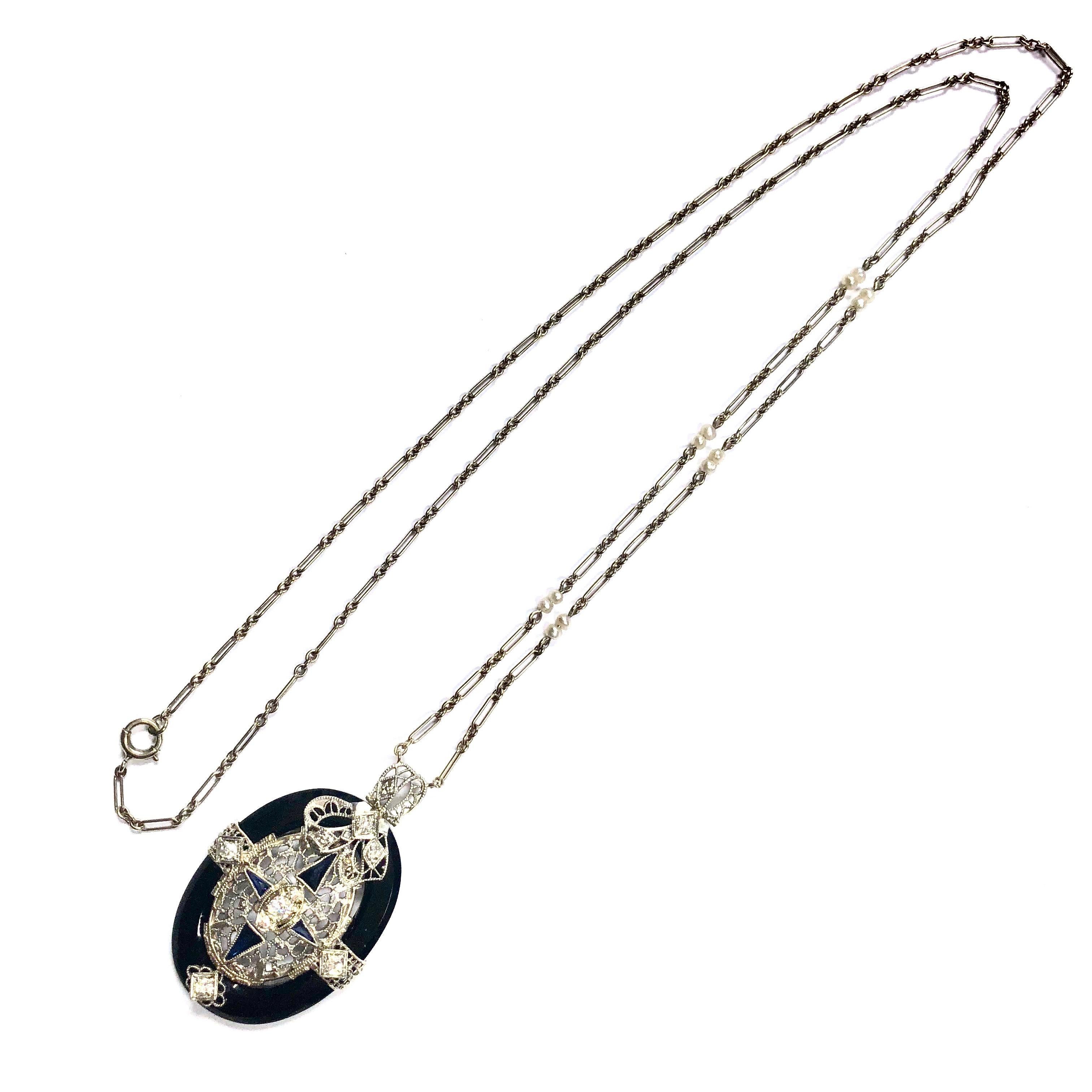 Crafted in 14K white gold, the necklace with an oval shaped pendant featuring a lace-like diamond and syntehetic blue sapphire set center set within a black onyx bezel, supported by a twenty-four inch chain terminating in a spring ring clasp. The