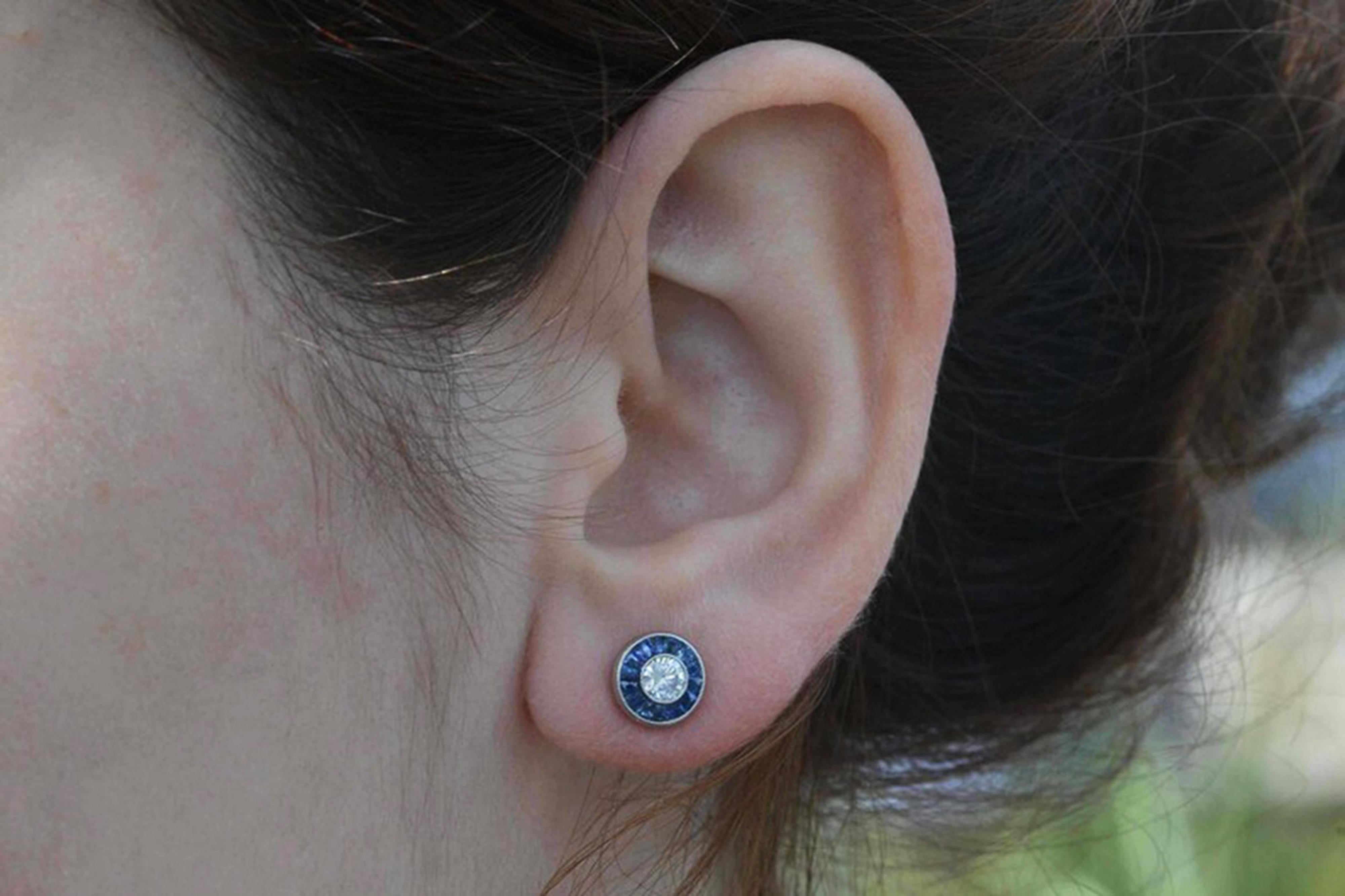An affordable pair of Art Deco style diamond stud earrings. The sizzling, 1/2 carat total weight round brilliant diamonds really sparkle and dance accompanied by a halo of velvety blue, natural sapphires. Called a target design due to the