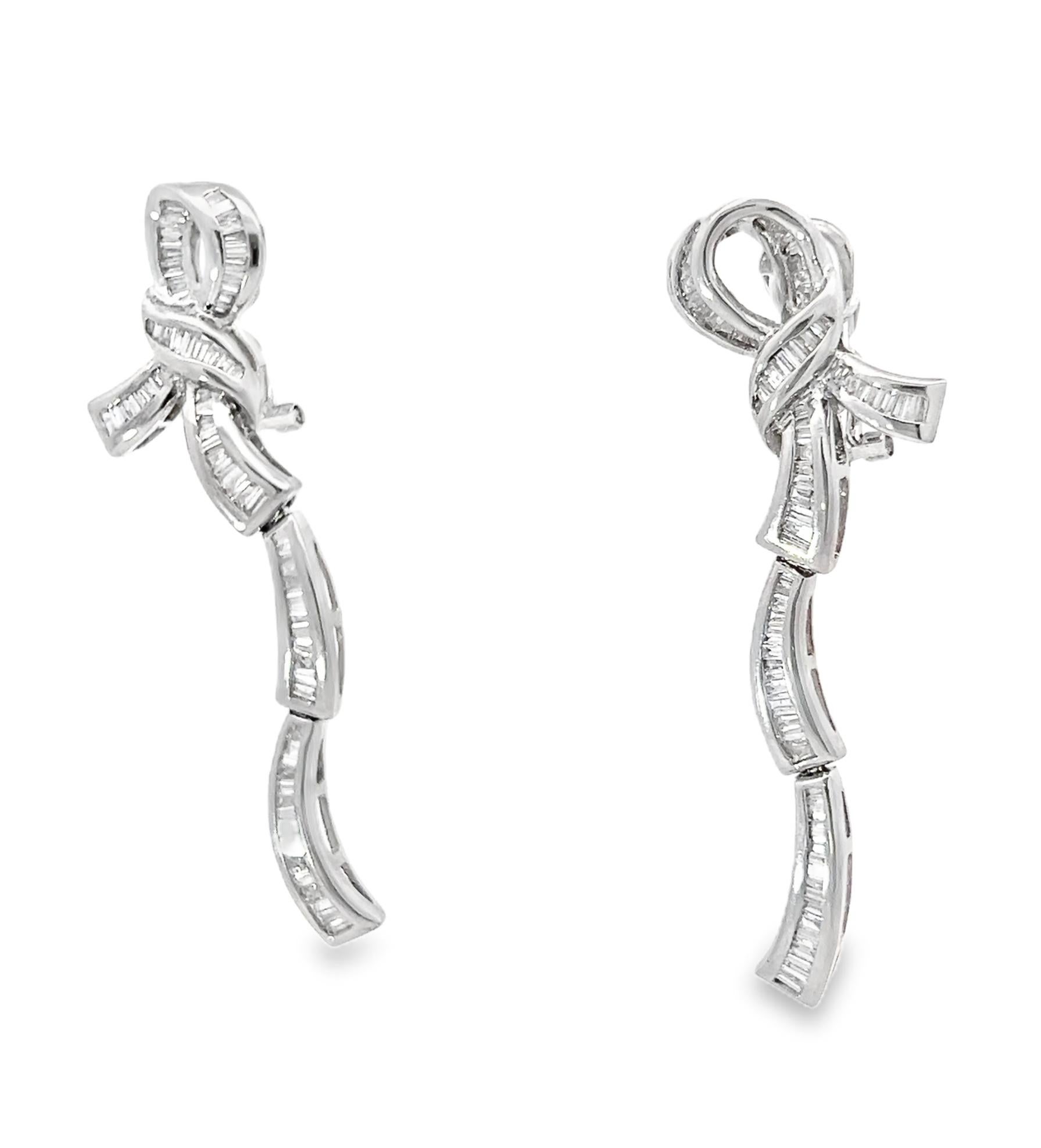 These exquisite Art Deco 18K white gold diamond bow drop earrings radiate vintage elegance with their sophisticated, cascading design. Crafted to capture light with every movement, they are channel-set with tapered baguette diamonds, creating a