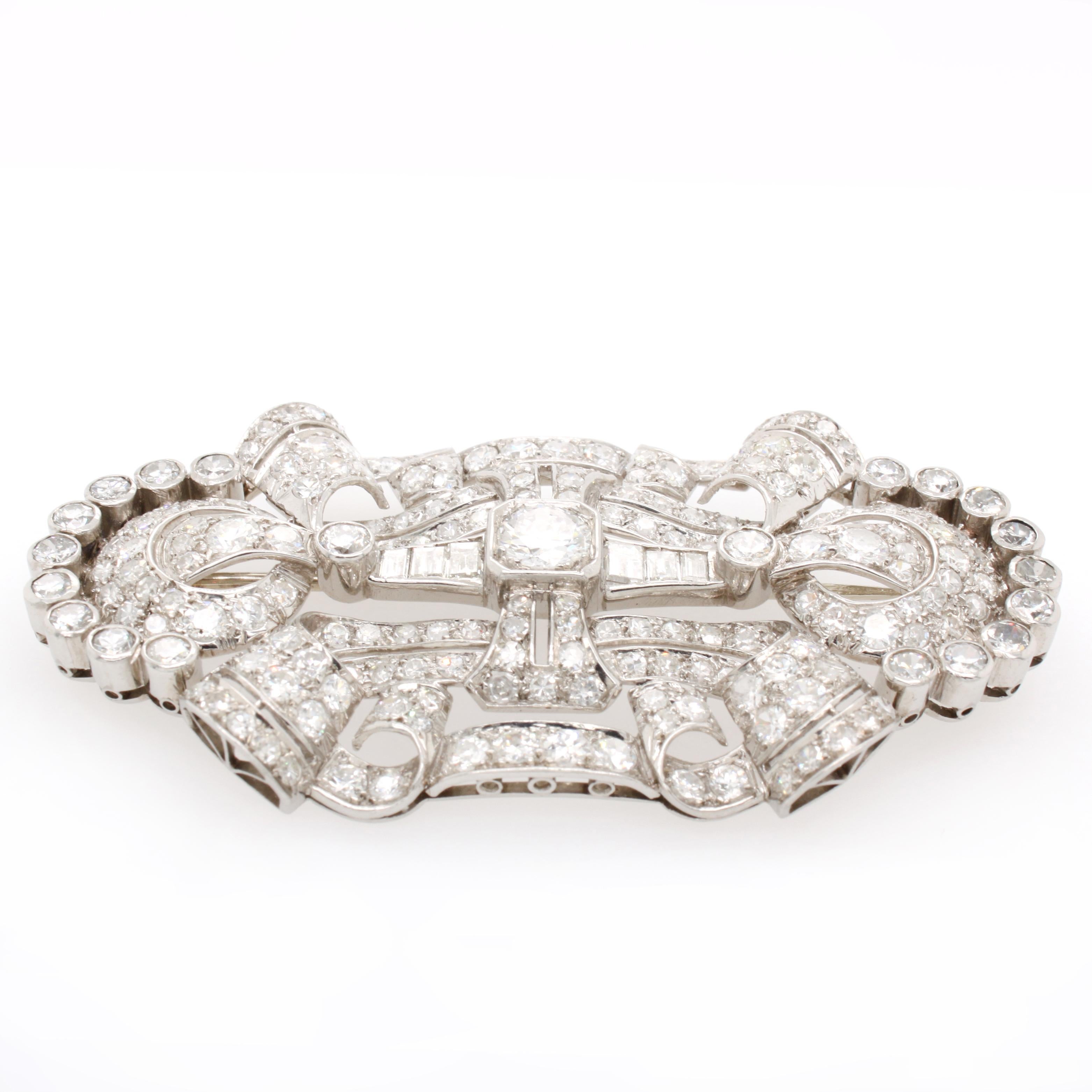 A French Art Deco diamond brooch in platinum, 1930s. The brooch is symmetrically designed with scroll and circular motifs, all leading to the centre brilliant cut diamond. The total diamond weight is approximately 10 carats consisting of mostly