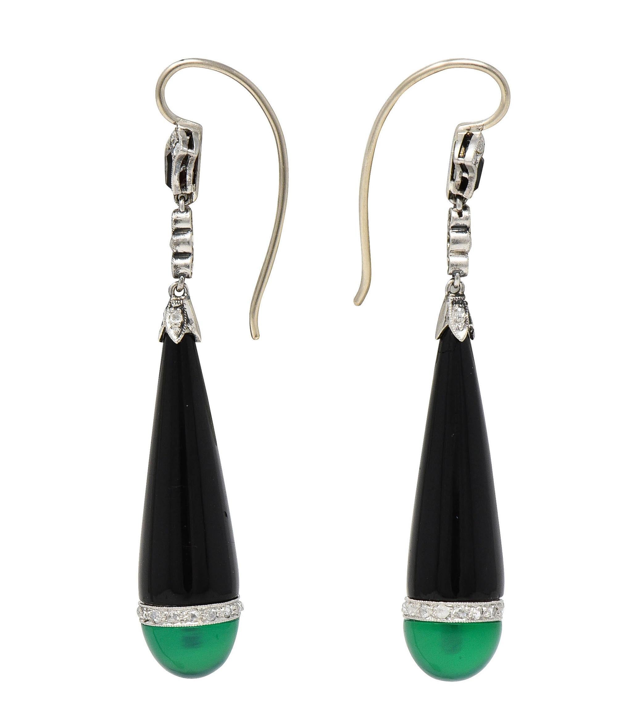Designed as spiculum-shaped drop earrings suspending from fanning lotus motif surmounts
Surmounts and drops are partially comprised of inlaid and carved onyx 
Semi-opaque to opaque dark reddish black to black in color
Drops terminate with 8.0 mm