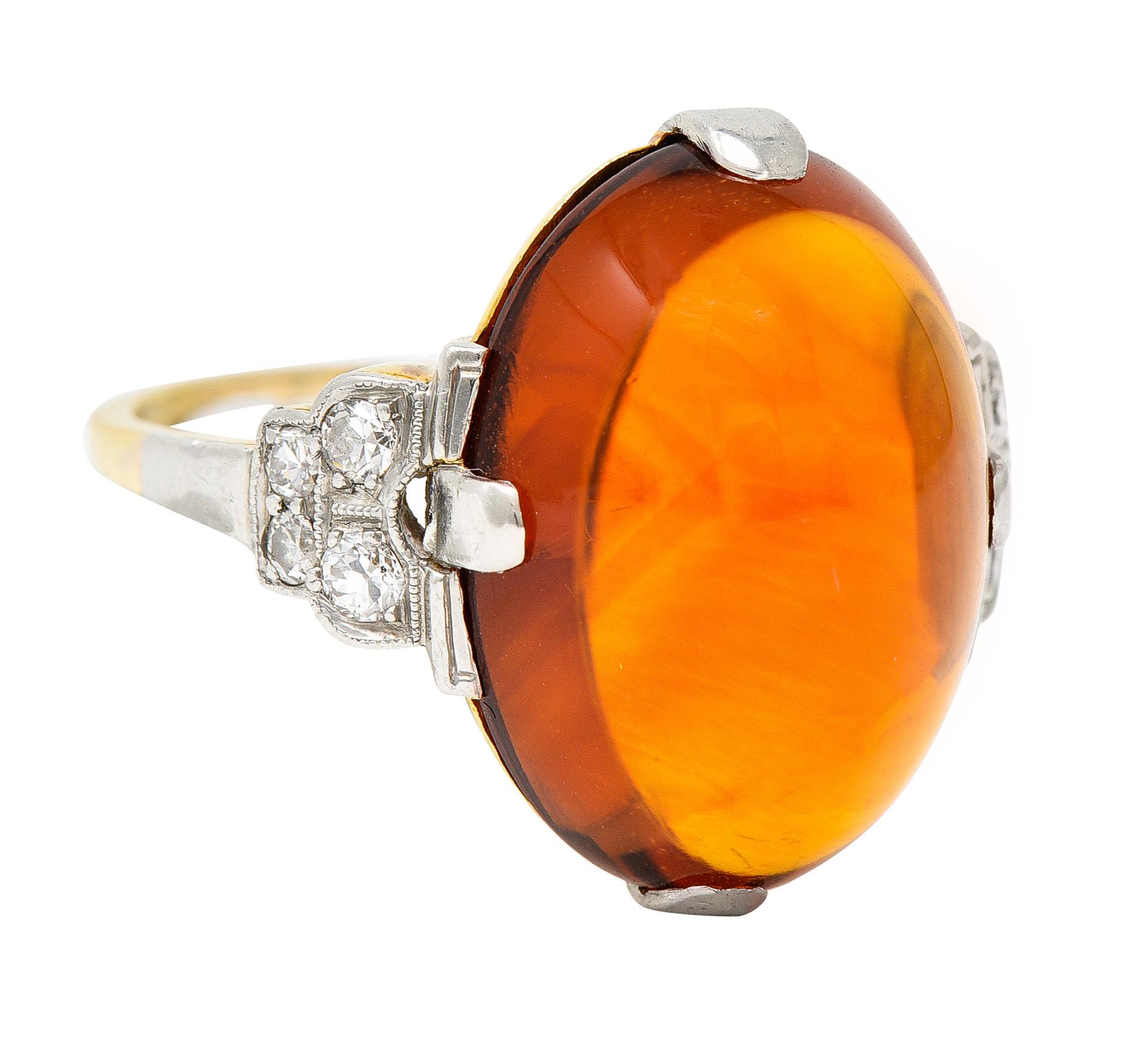 Centering an oval citrine cabochon measuring 13.0 x 18.0 mm - transparent medium reddish orange. Set with wide platinum prongs and flanked by platinum topped shoulders. With bead set single cut diamonds weighing approximately 0.30 carat total. Eye