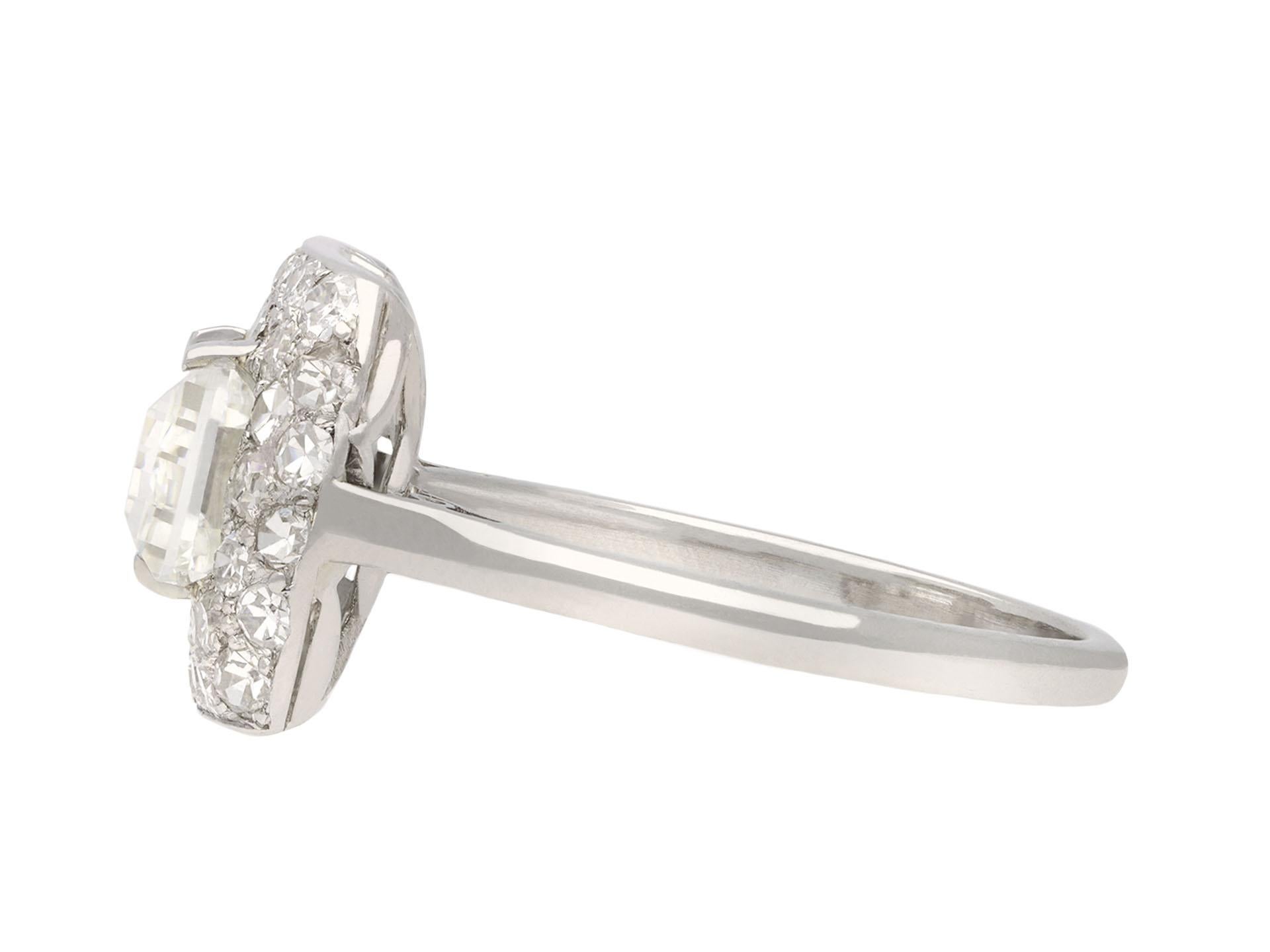 Art Deco diamond cluster ring. Set to centre with a rectangular step-cut diamond, J colour, S12 clarity, with a weight of 3.02 carats, in an open back claw setting, surrounded by forty-four round eight-cut diamonds in open back grain settings with a