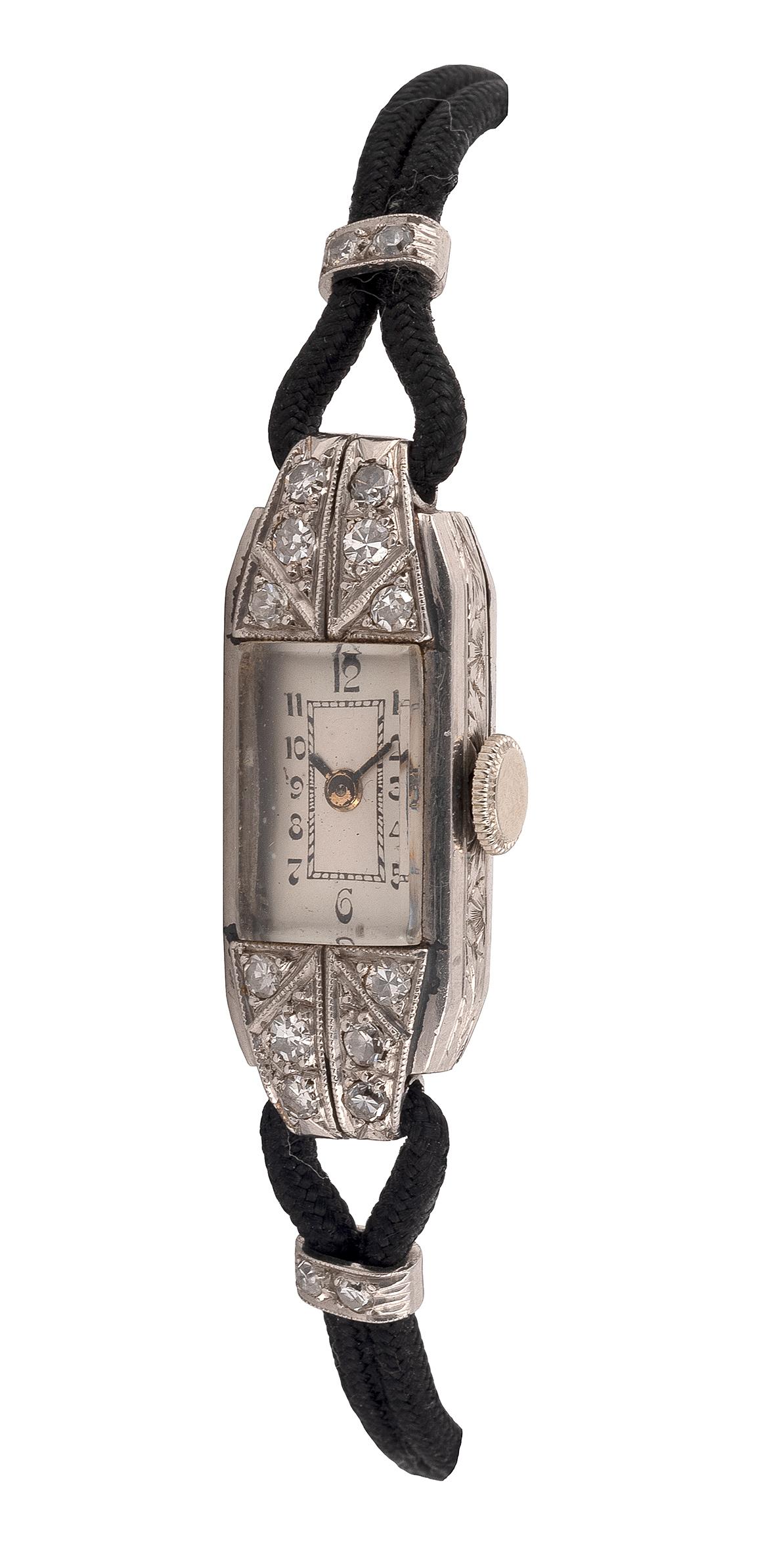 The rectangular dial with Arabic numerals with a single cut diamond bezel, between similarly-cut diamond lugs of geometric design, mounted in platinum, to a cord bracelet.
Lengths: 16.9cm