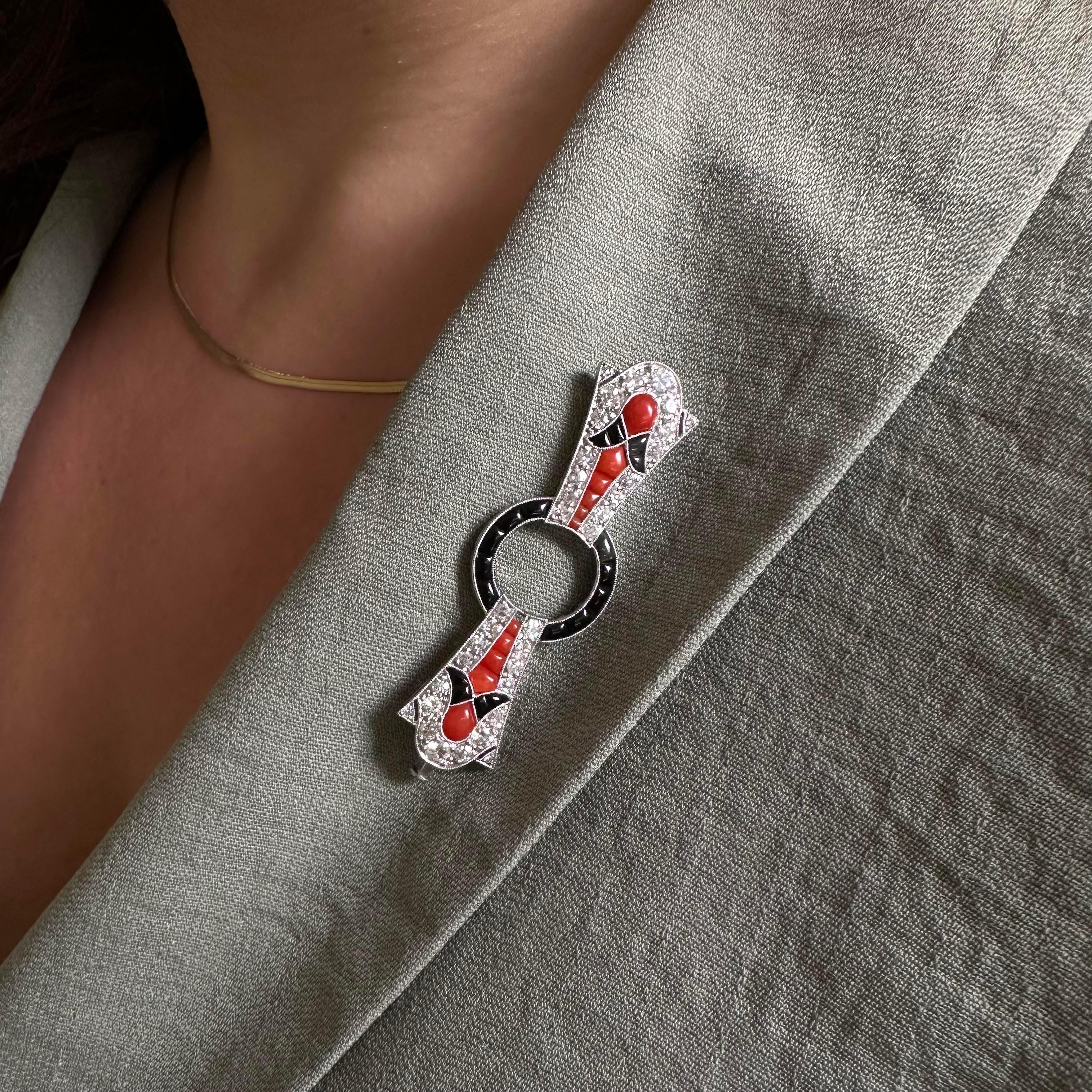 Spilla francese Art Déco in diamanti, corallo, onice nera e platino, con centro aperto e circolare, incastonato con onice nera a testa smerigliata, con ali a fiocco, grani incastonati con diamanti taglio otto, taglio vecchio e taglio brillante