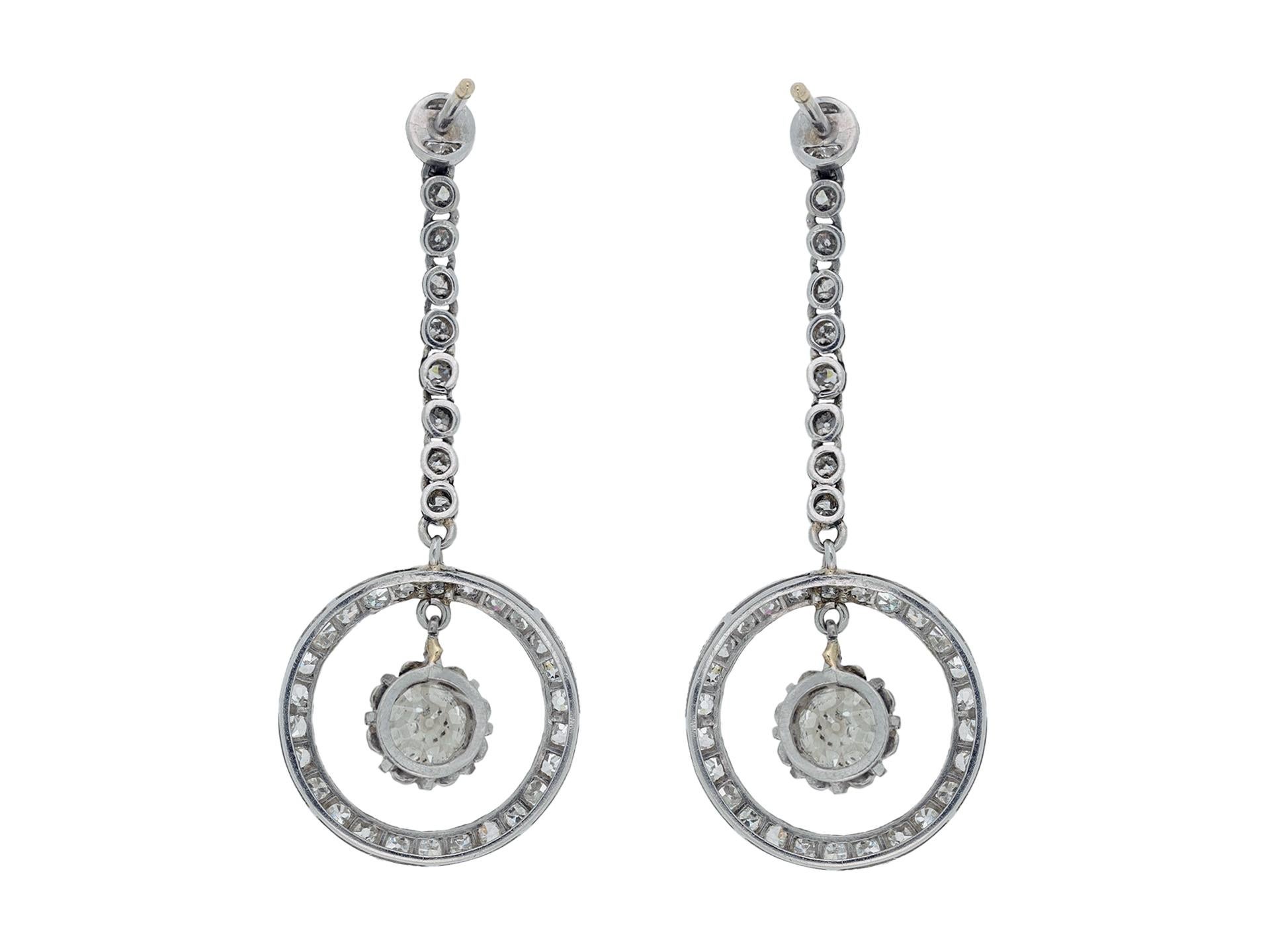 Art Deco diamond drop earrings. A matching pair, each set to center with a cushion shape old mine diamond in an open back claw setting, two in total, with a combined approximate weight of 1.25 carats, encircled by twenty-six round eight-cut diamonds