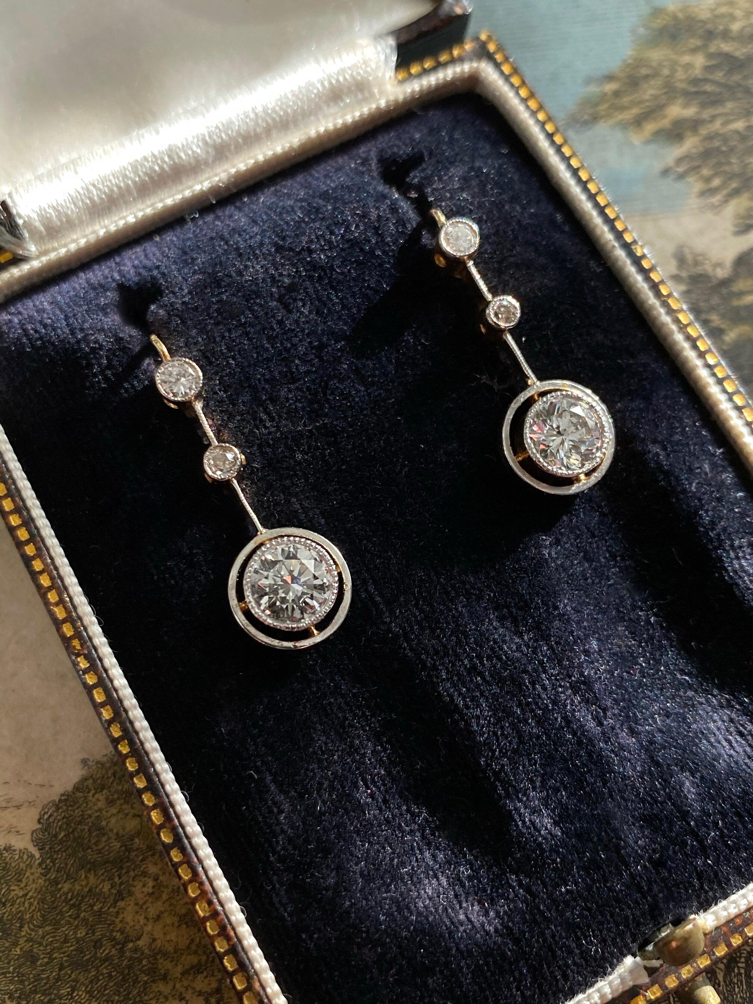 A pair of bright-white brilliant-cut diamonds float from within a platinum halo, gracefully suspended below an articulated row of diamonds. Circa 1930s, these lovely earrings are fabricated in platinum topped 18 karat yellow gold with leverback