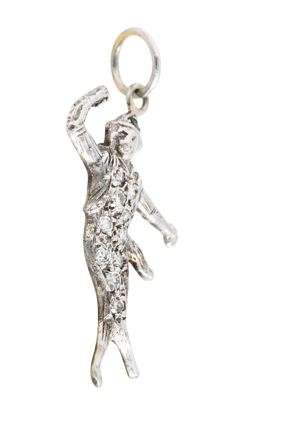 Charm is designed as a highly rendered dancer with a sashed belt, cropped jacket, and pointed hat. Body is pavè set with single cut diamonds while hat is accented by a round cut emerald. Total gemstone weight is approximately 0.18 carat. Tested as