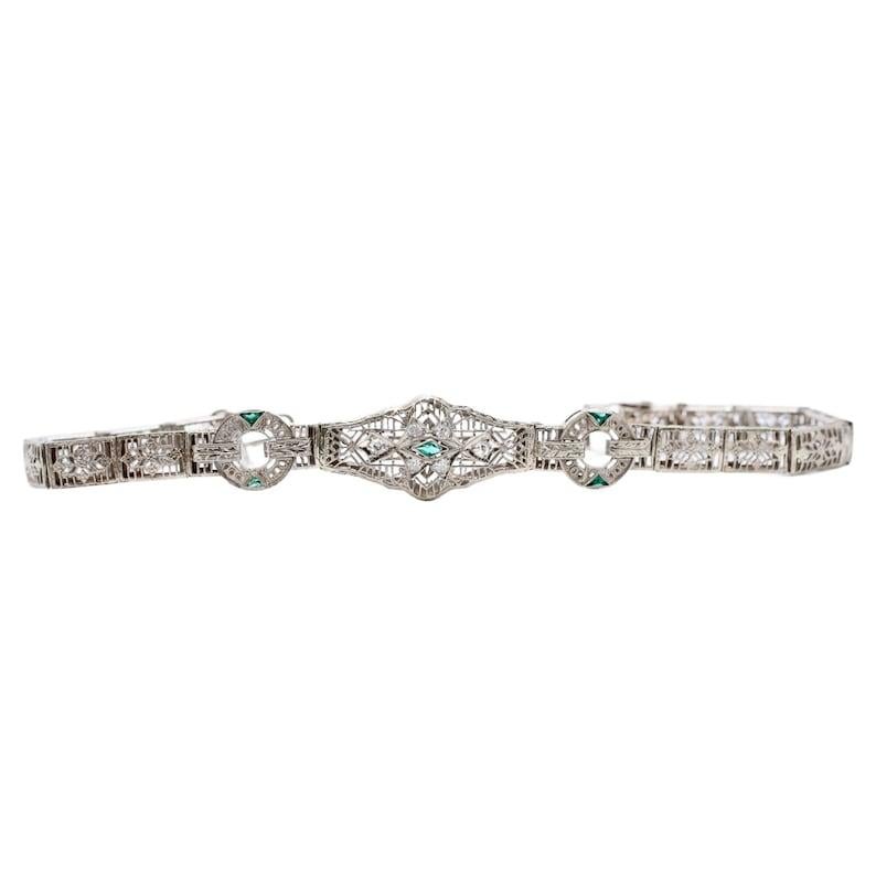 Aston Estate Jewelry Presents

An Art Deco period diamond and emerald filigree bracelet. Set with six diamonds of 0.18ctw with G color and VS clarity. Accented by five fancy shaped French cut synthetic emeralds of vivid green color. The filigree