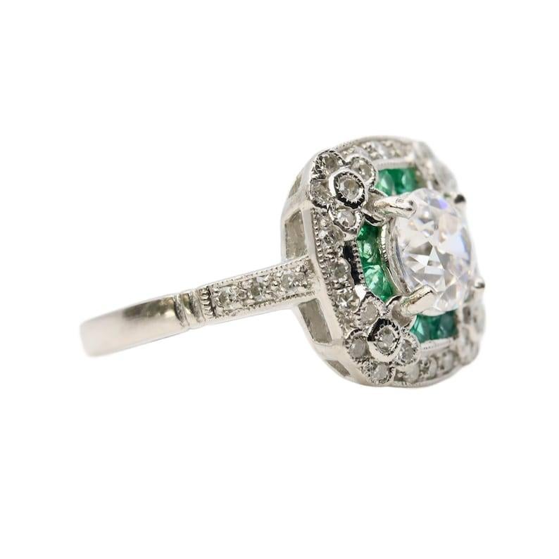 Aston Estate Jewelry Presents:

An Art Deco emerald, and diamond engagement ring in platinum. Centered by a 1.00 carat H color SI1 clarity old European cut diamond. Accented by four diamond set flowers, calibre cut emeralds, and pave set diamonds