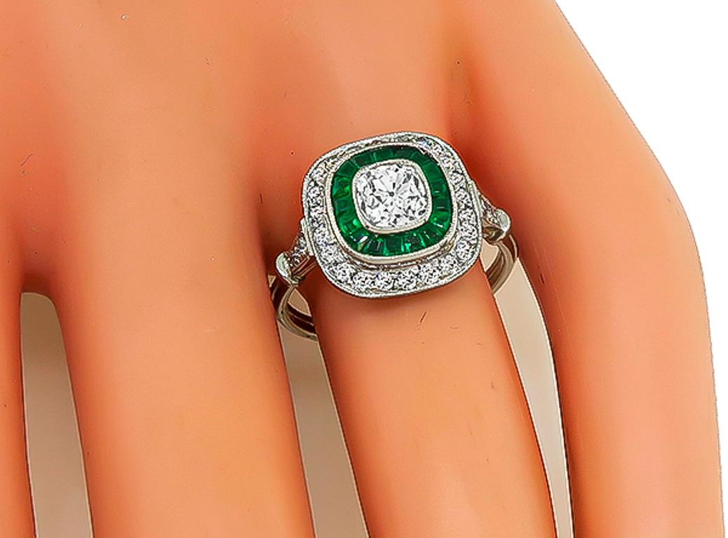 This amazing ring centers a sparkling cushion cut diamond that weighs approximately 0.75ct. graded H color with VS1 clarity. The center diamond is accentuated by round cut diamonds and calibre cut emeralds that weigh approximately 0.50ct and 0.50ct