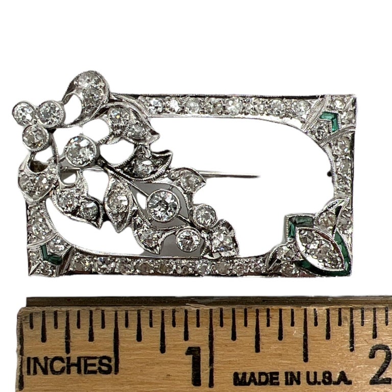 Original Art Deco diamond and emerald brooch handcrafted in platinum. The brooch features Old European cut diamonds weighing approximately 4.00 CTW and graded G-H color and SI clarity. The pin measures 1.75 x 1.00 inches. 