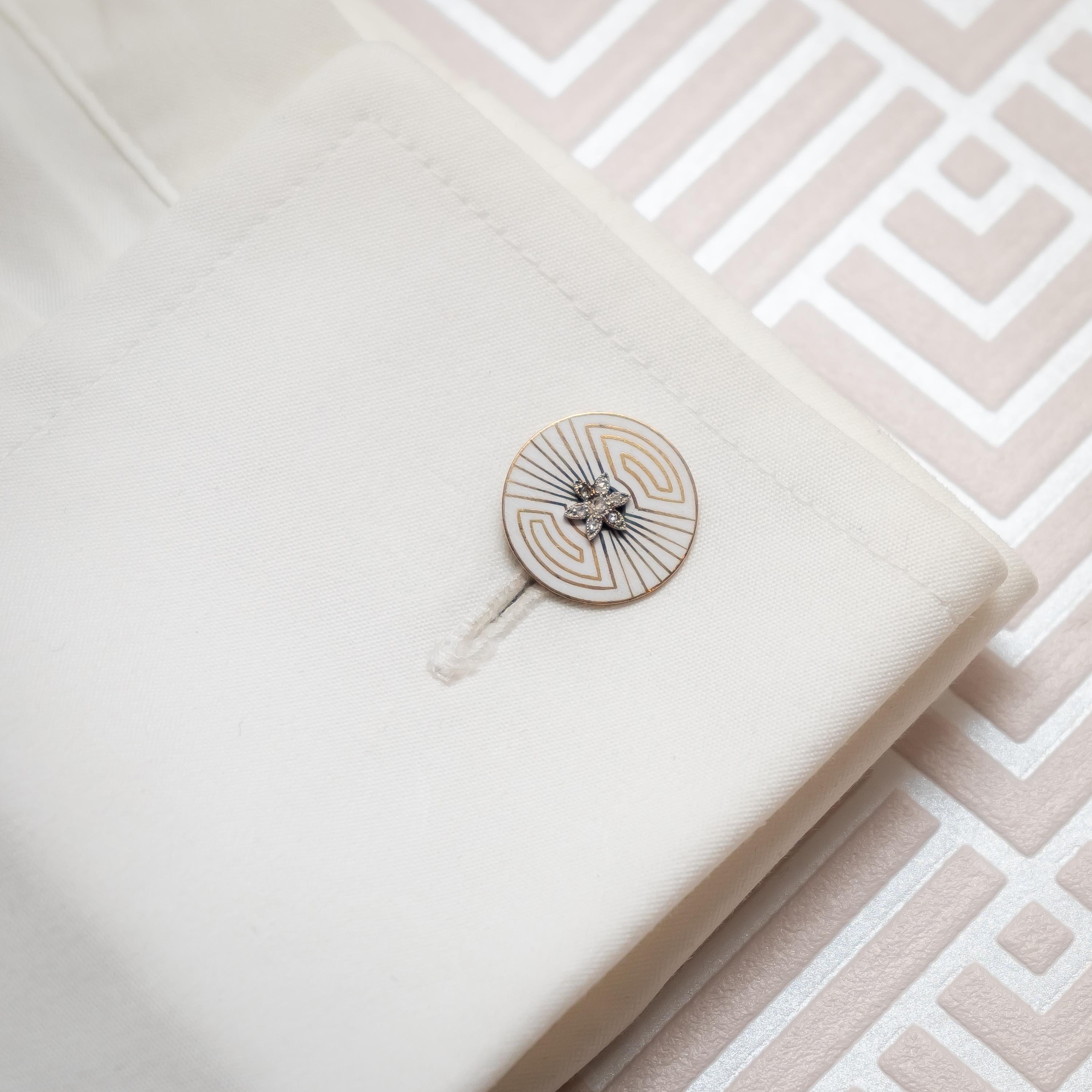 Une paire de boutons de manchette Art Déco, de forme circulaire, en émail blanc à motif géométrique, avec des diamants taillés en rose dans des sertissages de fleurs au centre, et des raccords de barre. Circa 1935.
