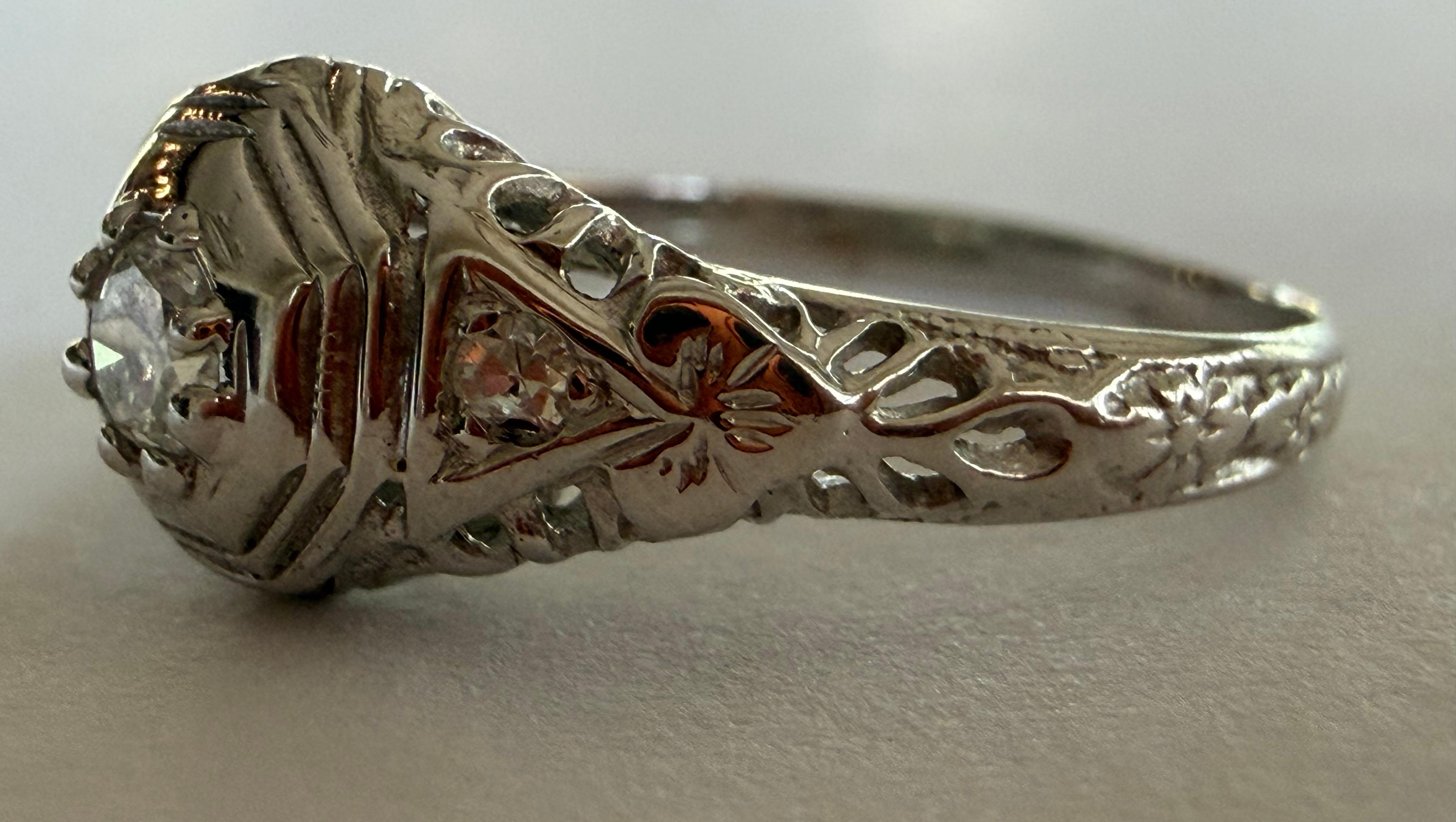 Un diamant de taille européenne ancienne mesurant environ 0,10 carats, de couleur F et de pureté VS, se trouve au centre de cette bague de fiançailles Art déco, accentuée par deux diamants de taille unique totalisant environ 0,04 carats et de fins