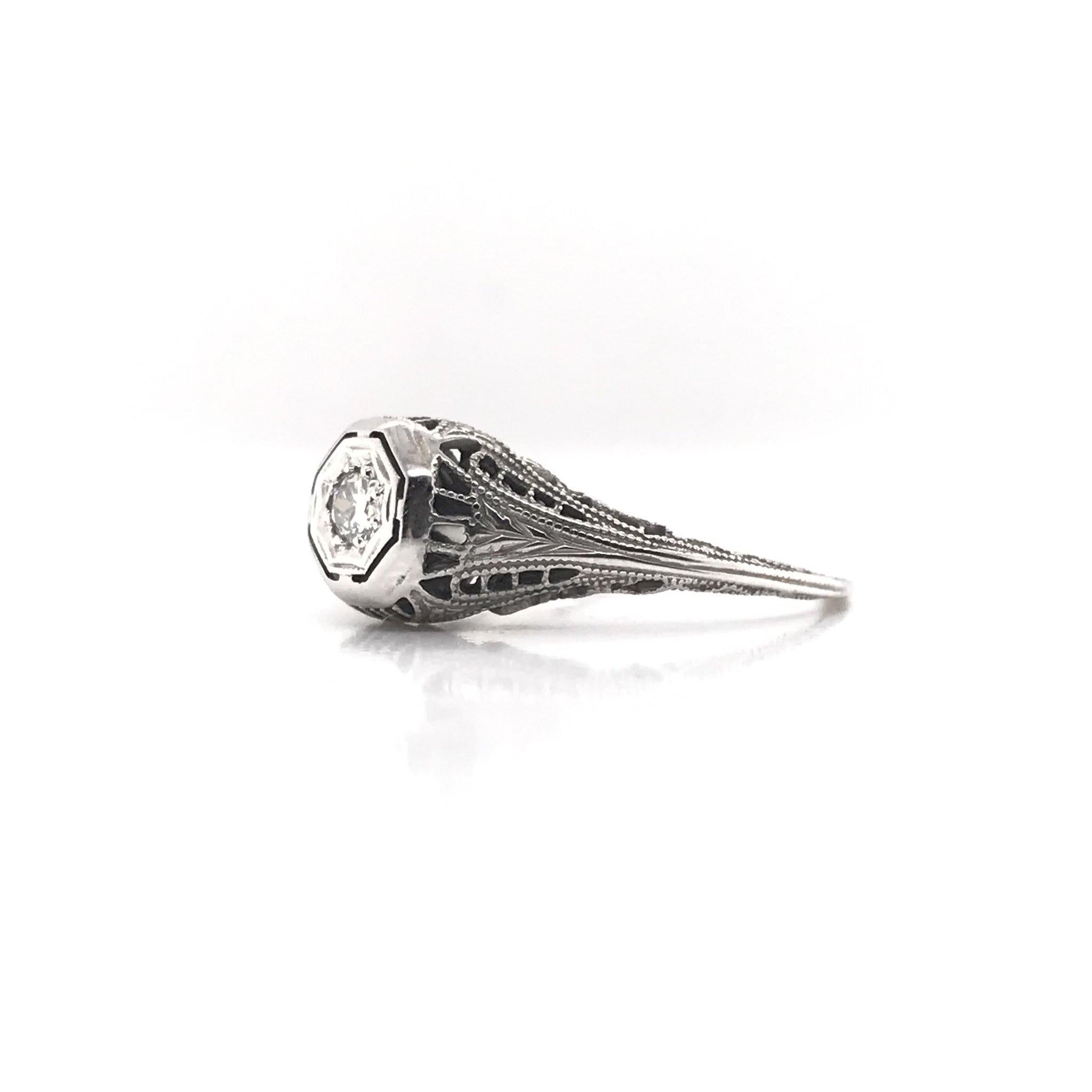 This piece was handcrafted sometime during the Art Deco design period ( 1920-1940 ). This petite filigree ring is a charming antique piece. It features a small 0.12 carat diamond in the center. The setting is 18k white gold. The setting features