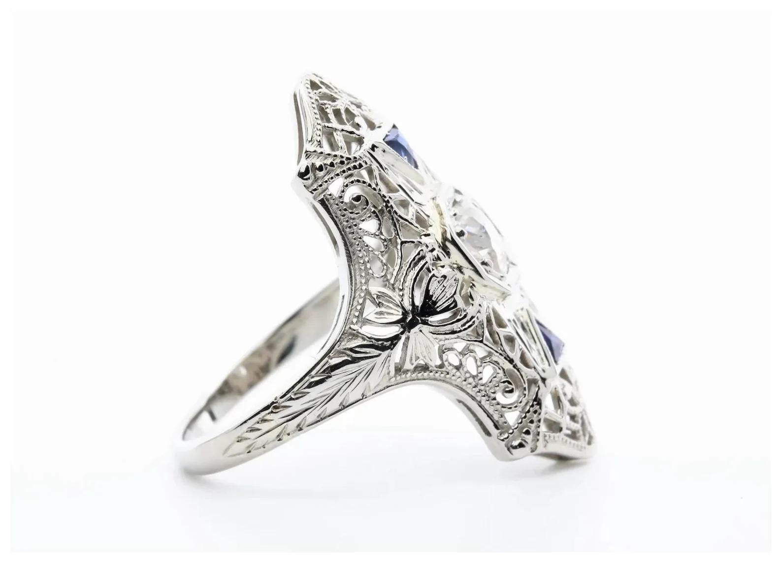 An Art Deco period old European cut diamond, and French cut sapphire cocktail ring. Crafted from 18 karat white gold, this ring features a 0.40 carat H color SI1 clarity old European cut diamond framed by a pair of French cut blue triangular