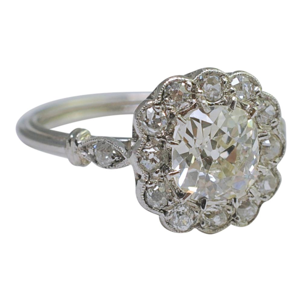 Art Deco era platinum and diamond halo engagement ring; this pretty ring has an Old European Cut diamond weighing 1.10ct set in the centre, surrounded by further Old European Cut diamonds totalling 0.40ct. The central diamond is a cushion shape and