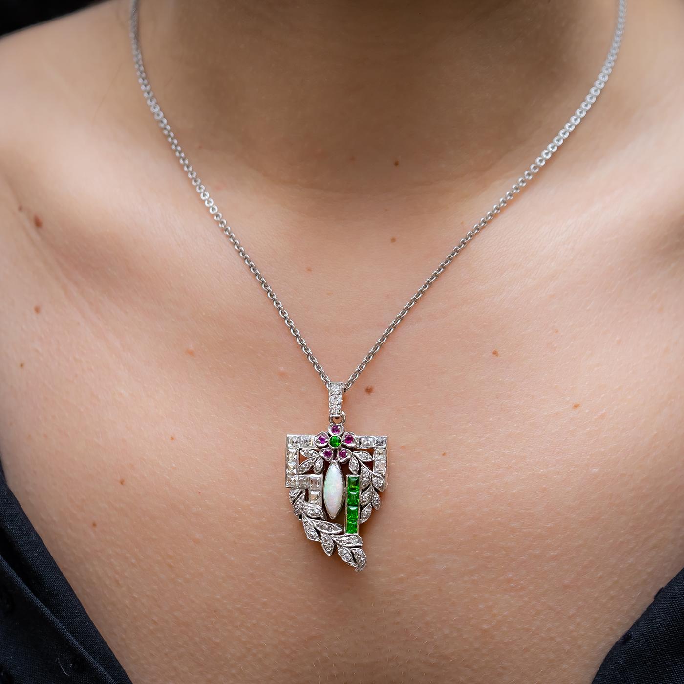 An Art Deco pendant, mounted in platinum, set with French-cut and old eight-cut diamonds, a cabochon marquise shaped opal, baguette and round cut demantoid garnets and round rubies. Estimated total diamond weight 0.90ct. The pendant measures