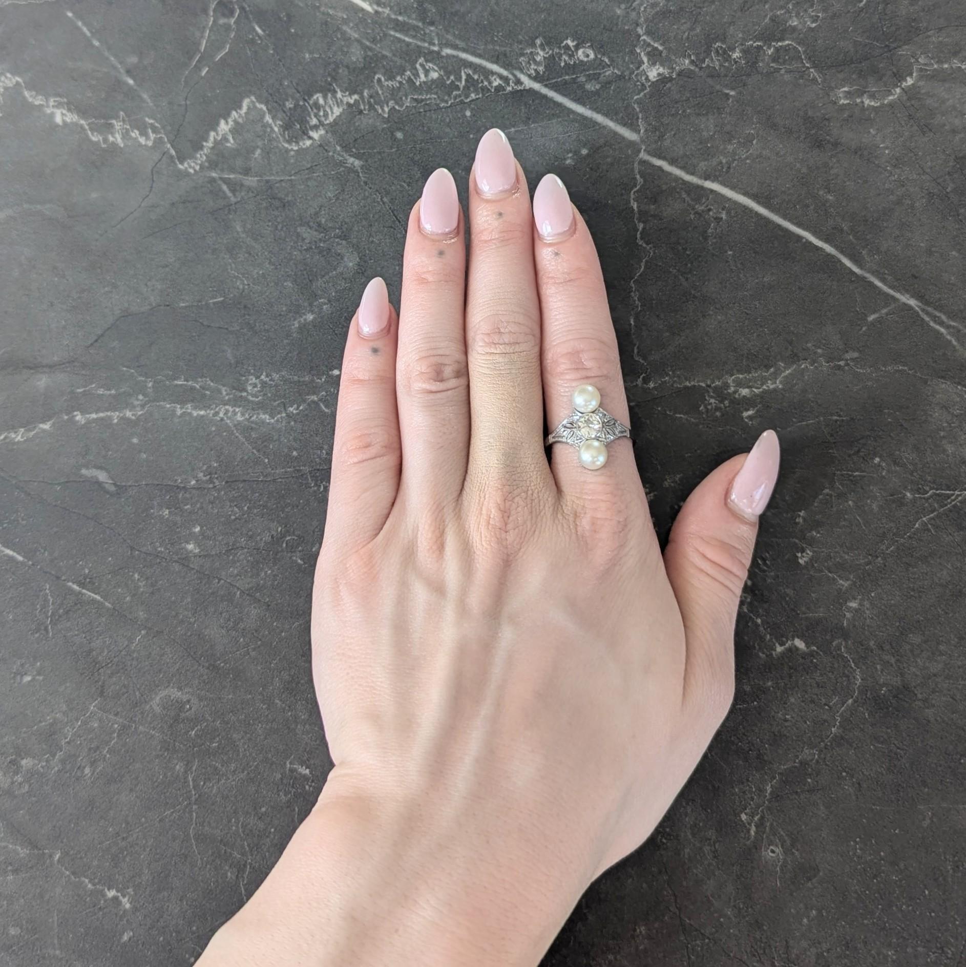 Centering an old European cut diamond bezel set in a navette form head
Weighing approximately 0.45 carat total - J color with VS2 clarity
Flanked north to south by 6.5 mm round pearls
Cream in body color with strong iridescence
Accented by pierced