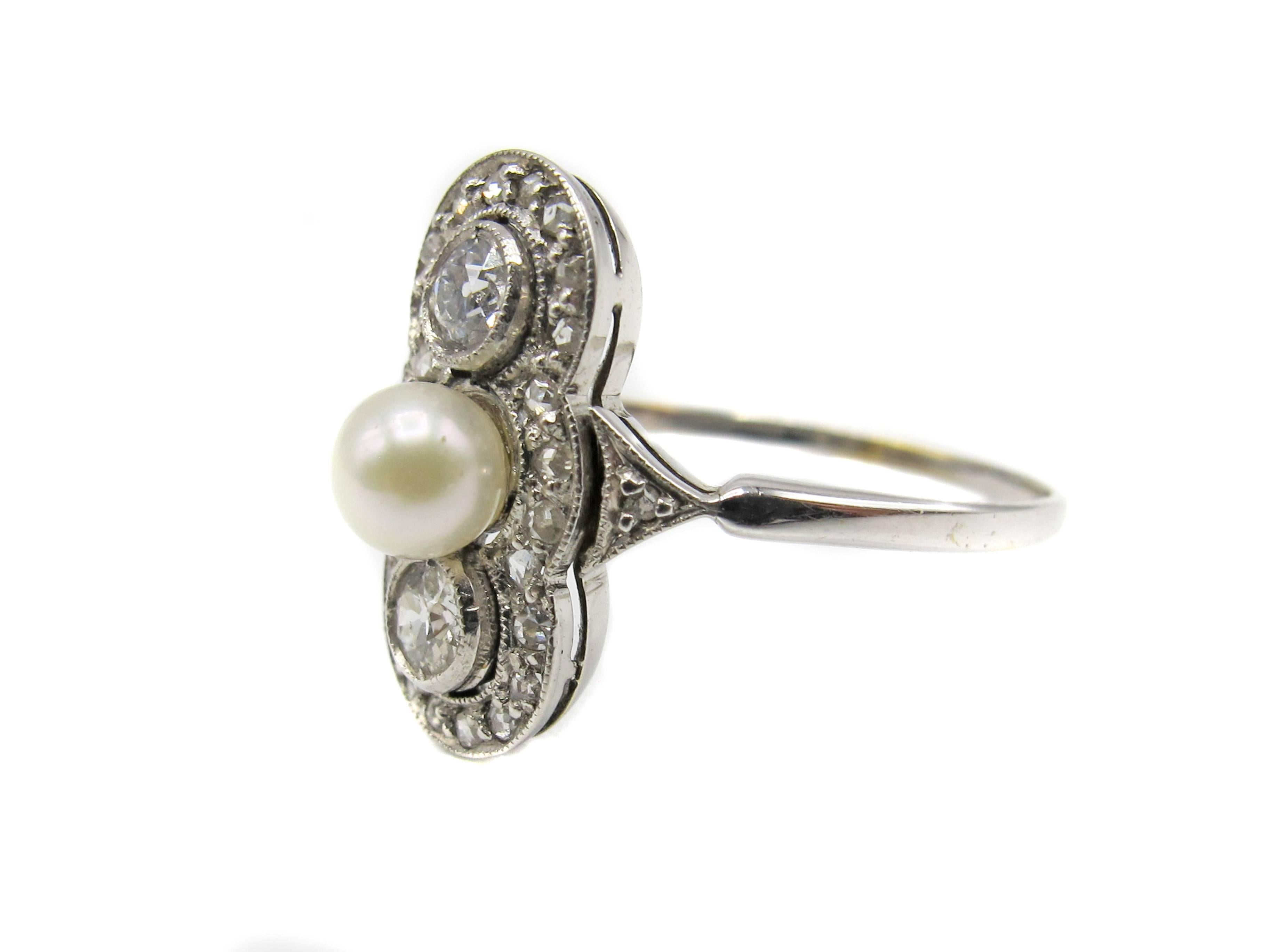 Charming Art-Deco 14 karat white gold diamond and pearl ring, centrally set with one white round pearl and flanked by 2 Old European Cut diamonds. Surrounding these, in a mill-grain bezel are 24 rose cut diamonds and another rose cut diamond on the