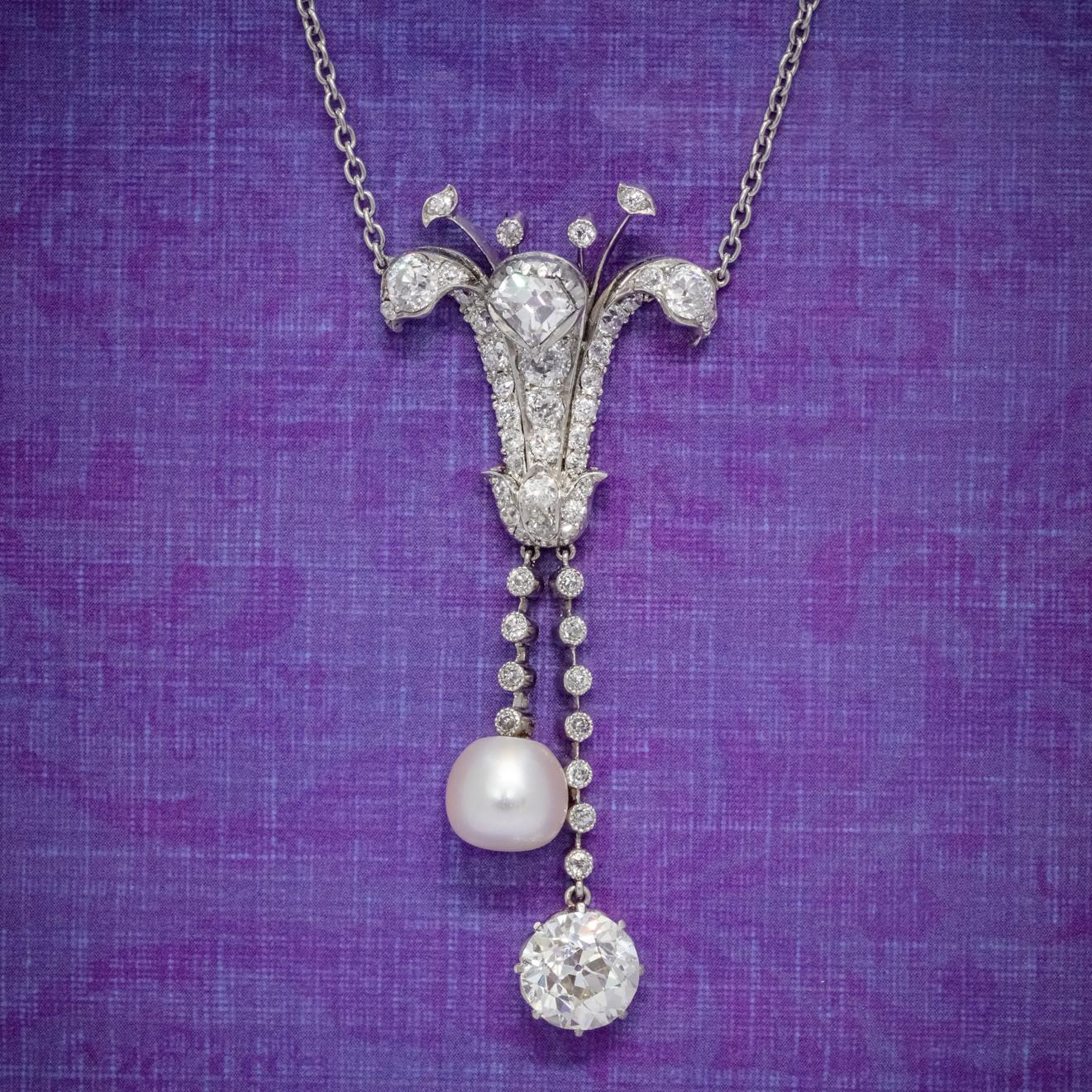 A magnificent Art Deco lavaliere necklace boasting a stunning lily shaped pendant with two droppers dangling from the bottom. Each dropper is lined with diamonds and lead to a large, natural saltwater pearl and a glorious old European cut diamond