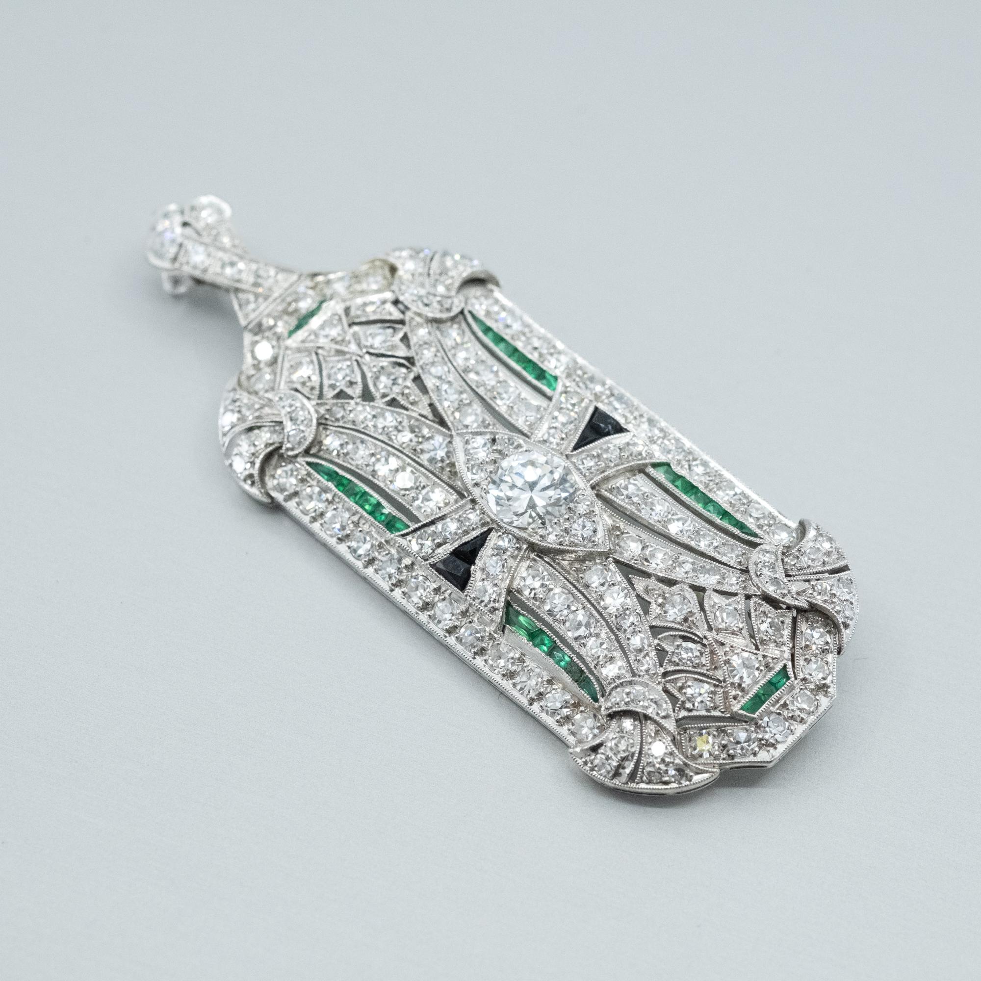 Un pendente con diamanti, smeraldi e onice, realizzato anche come spilla, in platino. 

Caratteristiche del diamante centrato: taglio rotondo brillante di circa 0,80 carati
Caratteristiche degli altri diamanti: grezzi, taglio a rosa o taglio