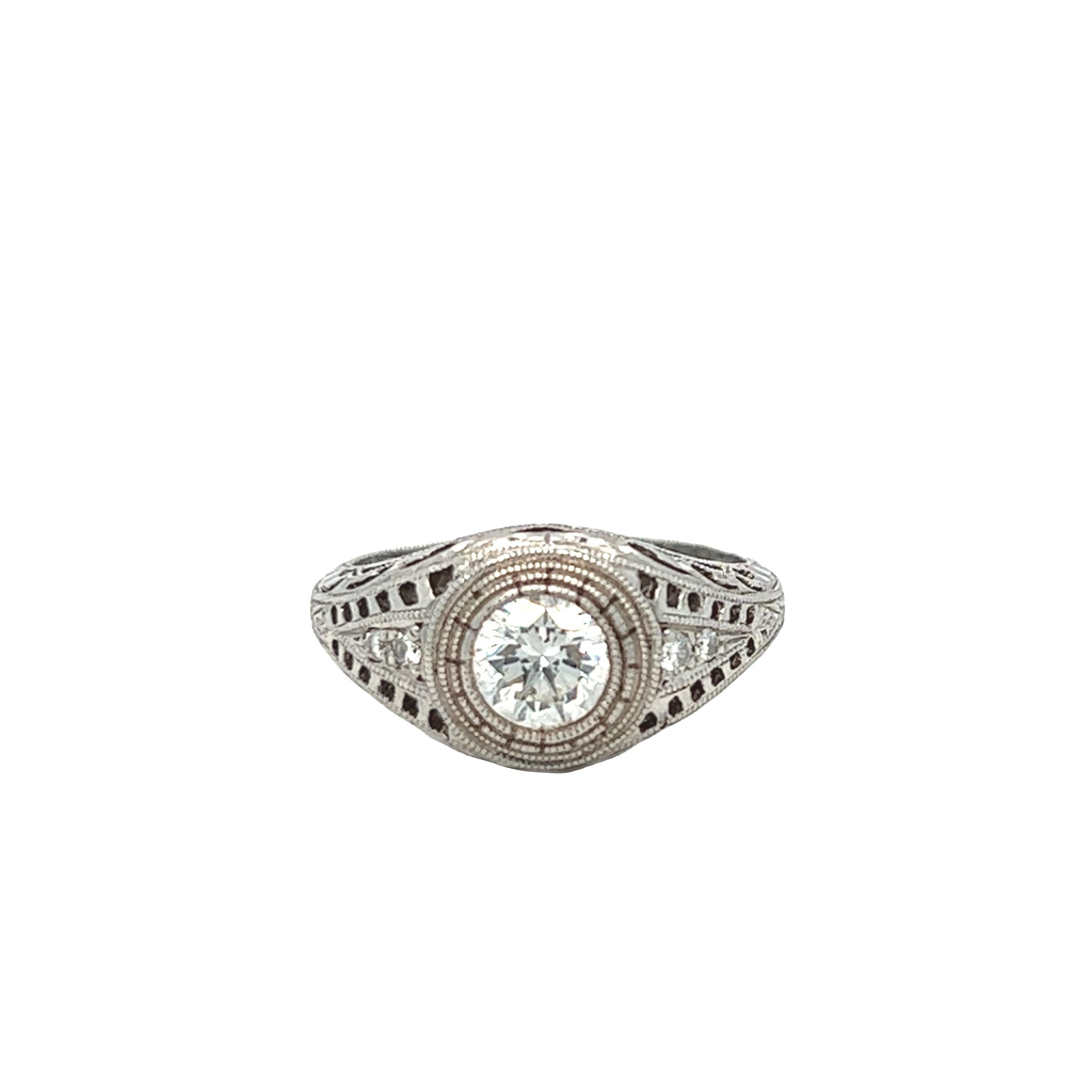 This platinum ring has a gorgeous cut out work and beautiful flowing filigree pattern all around the ring. The center stone is a round cut 0.85 ct with G color and SI clarity. The unique design wraps around 4 accent diamonds about 0.10 carat total.