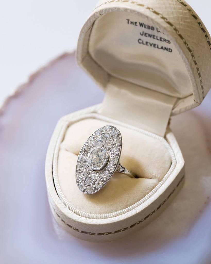 This is a dazzling and authentic Art Deco (circa 1925) platinum navette style ring. This fabulous sparkler centers a bezel set antique Cushion Cut diamond, acompanied by a UGS appraisal stating stone is gauged at approximately 1.06ct, graded G-H in