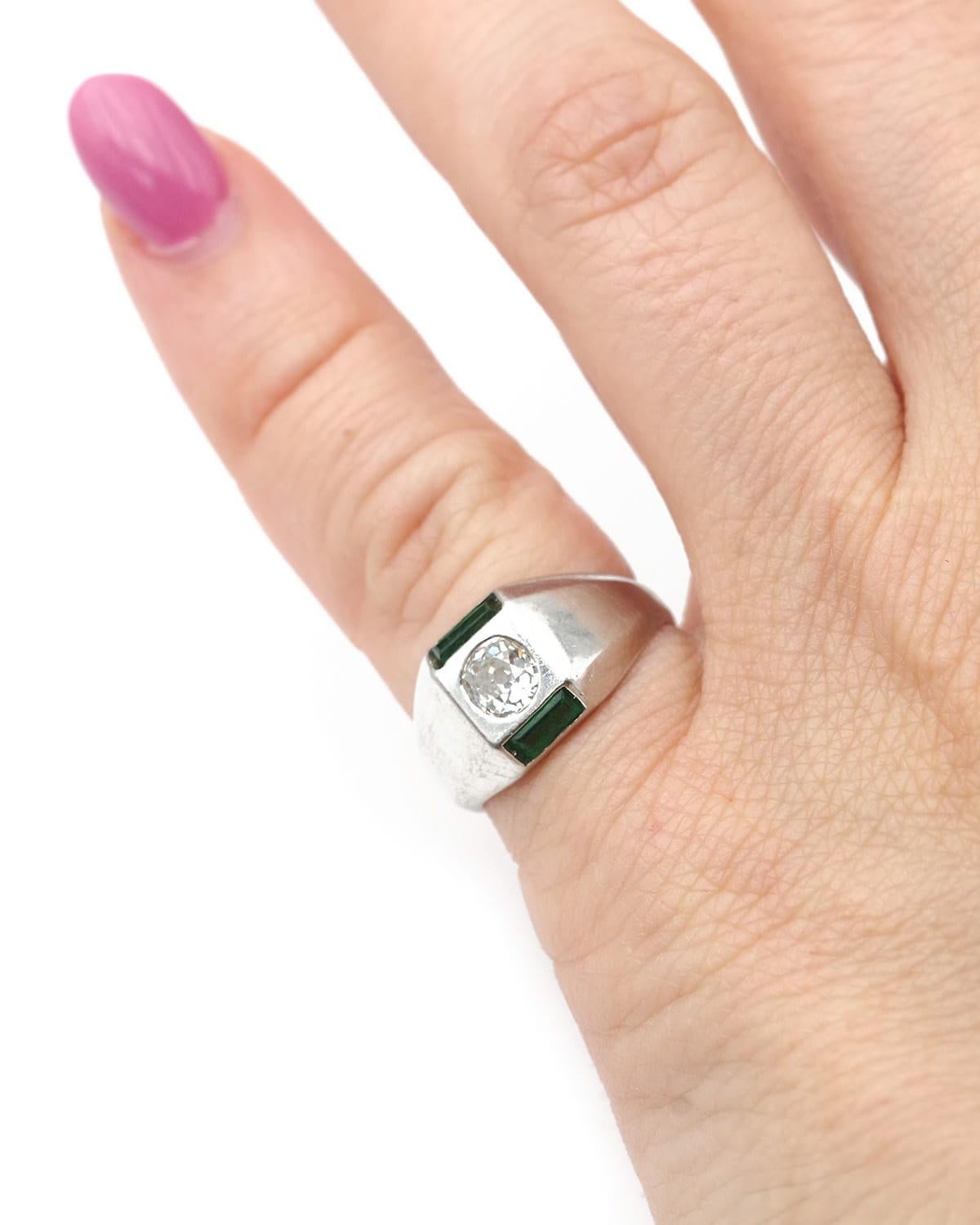 Art Deco diamond signet ring in platinum. Little finger signet ring featuring a 0.30 carat old-cut diamond in its center. On either side, a baguette-cut emerald and green glass frame the center diamond. Its geometric design embodies the