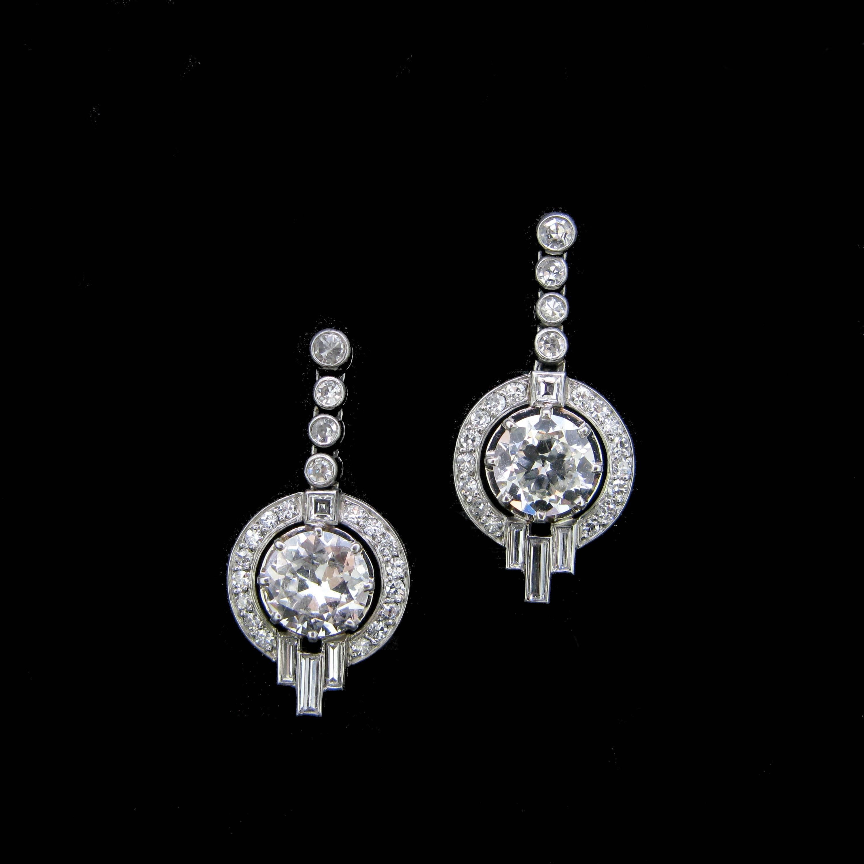 This beautiful pair of dangling earring si from the Art Deco era with its geometric shape. They are made in both 18kt white gold and platinum and are set with two main round brilliant cut diamonds each weighing 1.40ct and then surrounded by smaller