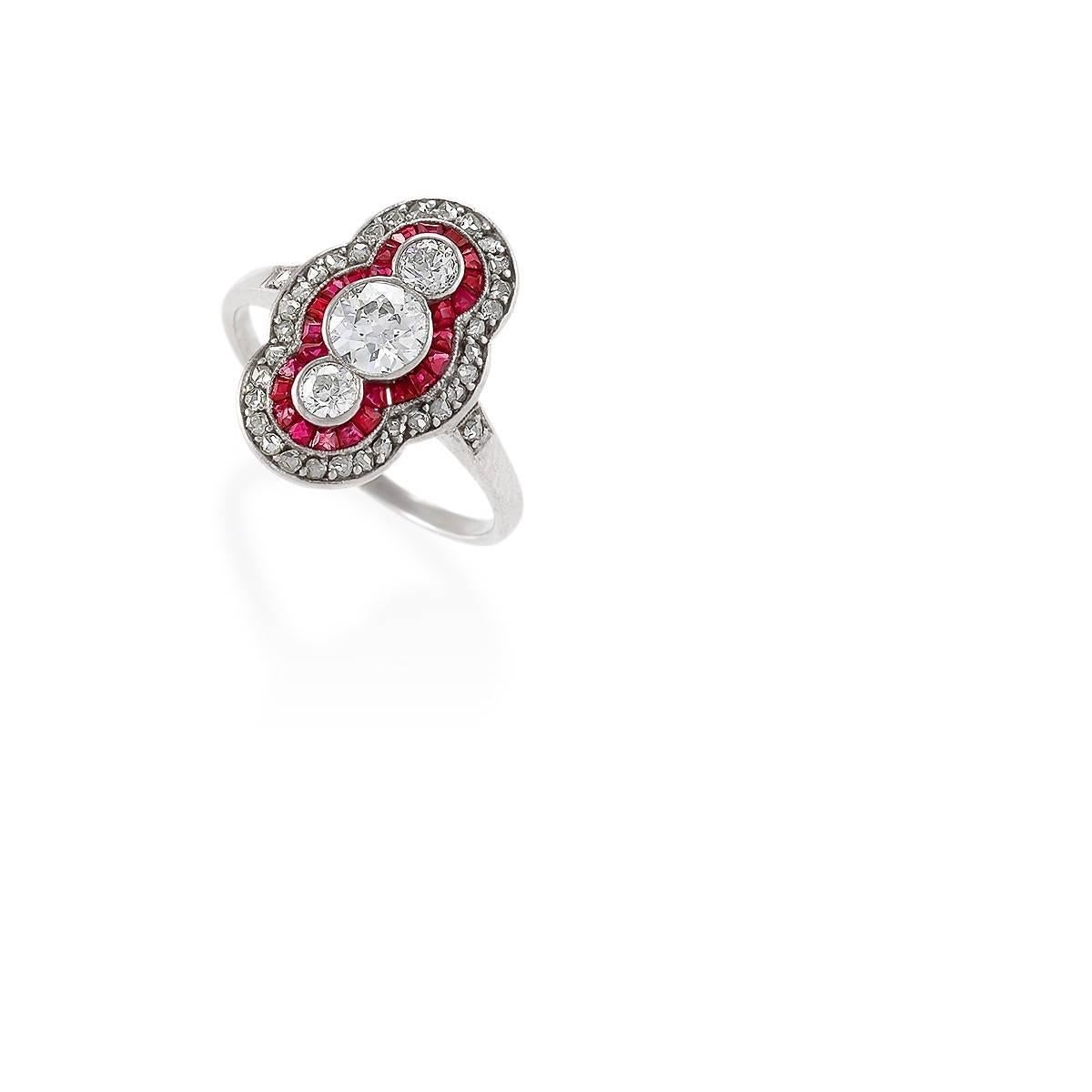 An Art Deco platinum and 14 karat ring with diamonds and rubies. The ring is designed in a classic platinum-on-gold plaque motif, with the 3 larger diamonds architecturally framed by a middle halo of ruby, which is further accented with a ring of