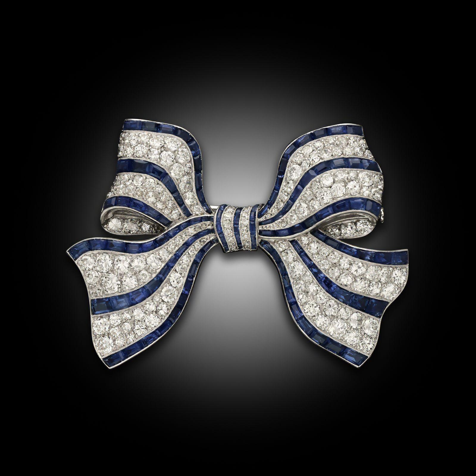 An Art Deco diamond and sapphire bow brooch, crafted in platinum, circa 1920. The bow is designed with stripes of old cut diamonds and calibre cut sapphires all set in platinum. The realistic design of the bow undulates with dimension and fastened