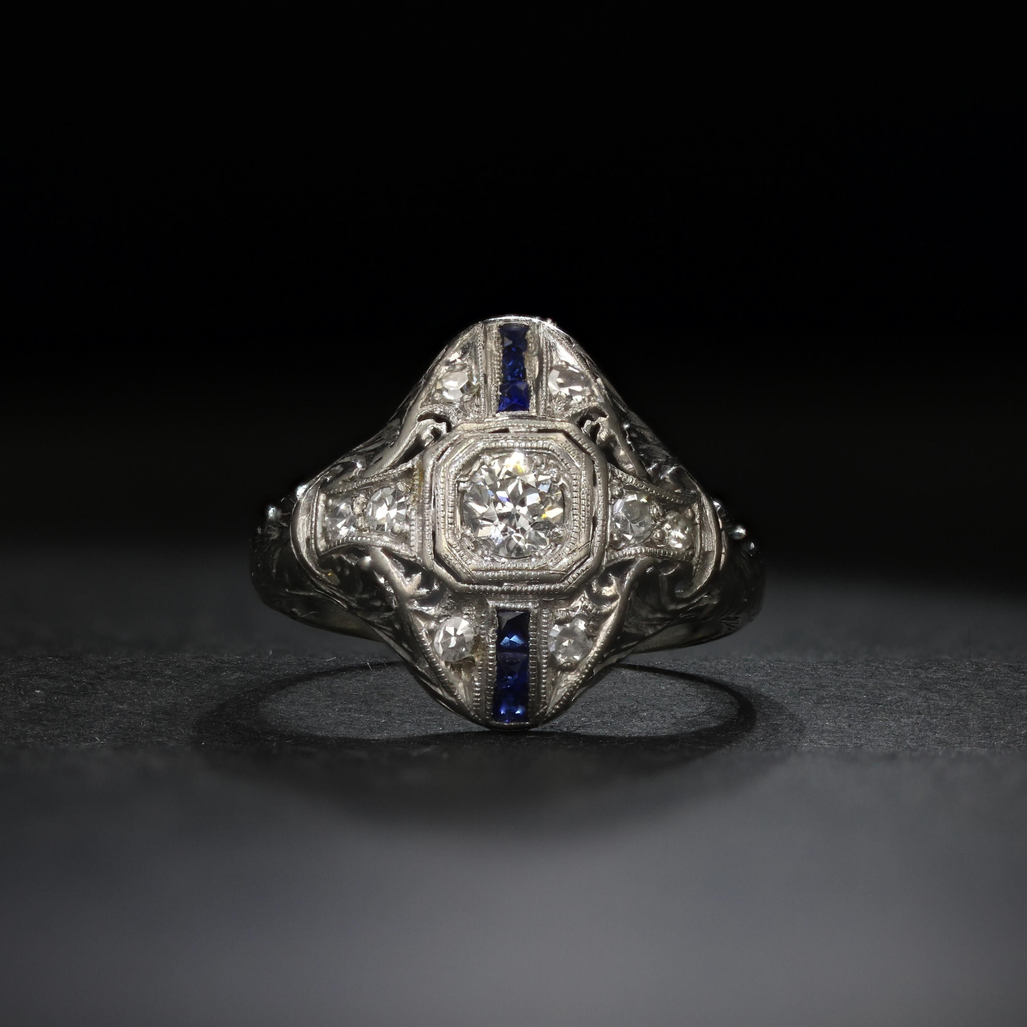 In the center of this gorgeously engraved platinum ring is an old mine diamond of half a carat. Several more old mine diamonds enrich the top of this artfully crafted ring. Accentuating the diamonds is a column of square-cut sapphires, adding a