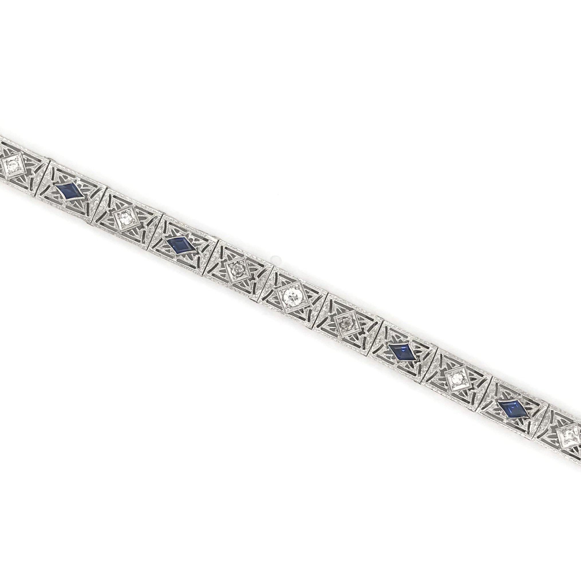 This antique piece was handcrafted sometime during the Art Deco design period ( 1920-1940 ). The setting is 10k white gold. The bracelet is comprised of 18 filigree links, 7 of which have a small diamond accent and 4 have a deep blue sapphire