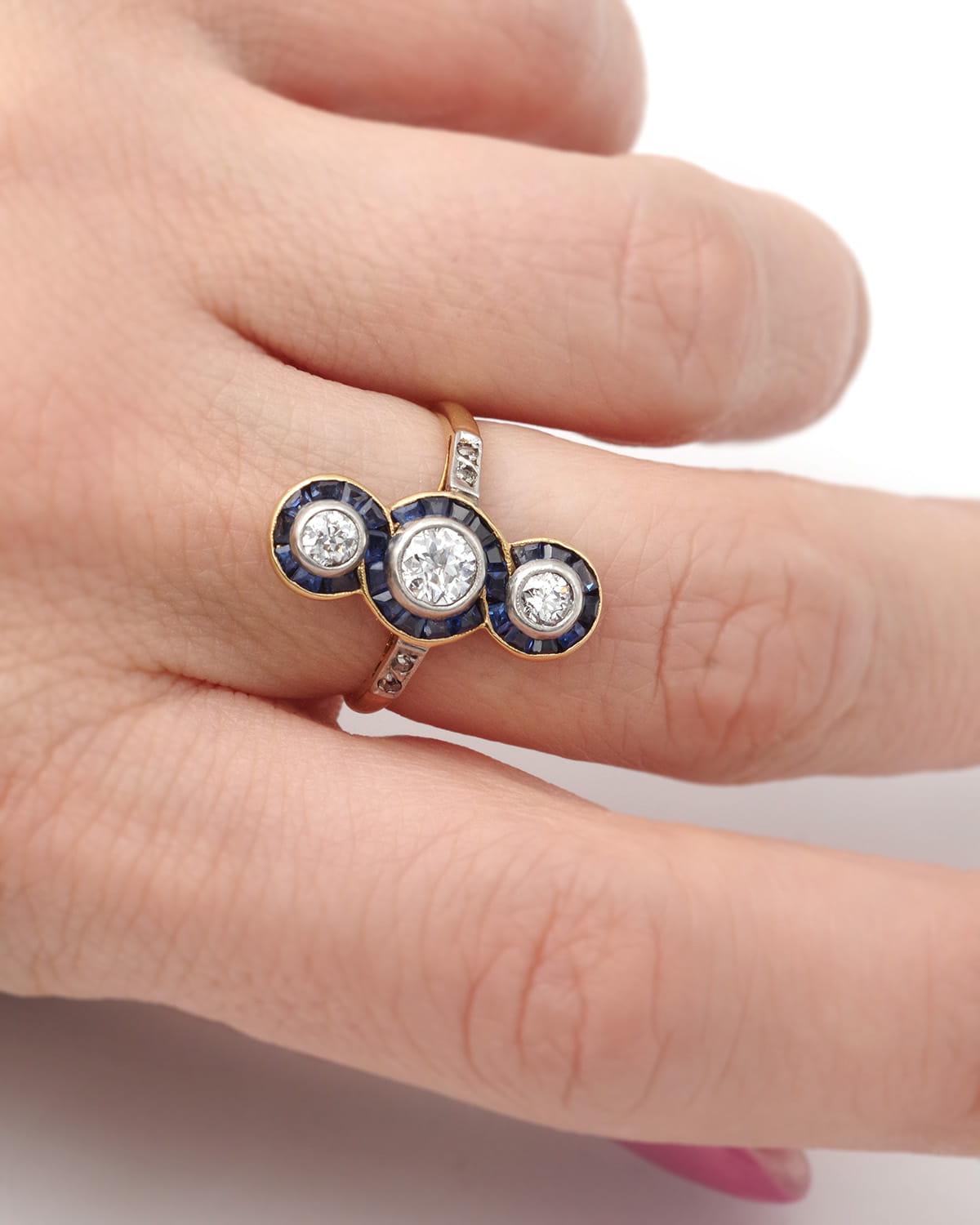 Anello lungo con diamante e zaffiro Art Deco in oro 18 carati e platino. Anello allungato, ornato da tre diamanti taglio vecchio di 0,10, 0,30 e 0,10 carati, in montatura. I diamanti sono circondati da zaffiri naturali calibrati, che formano linee