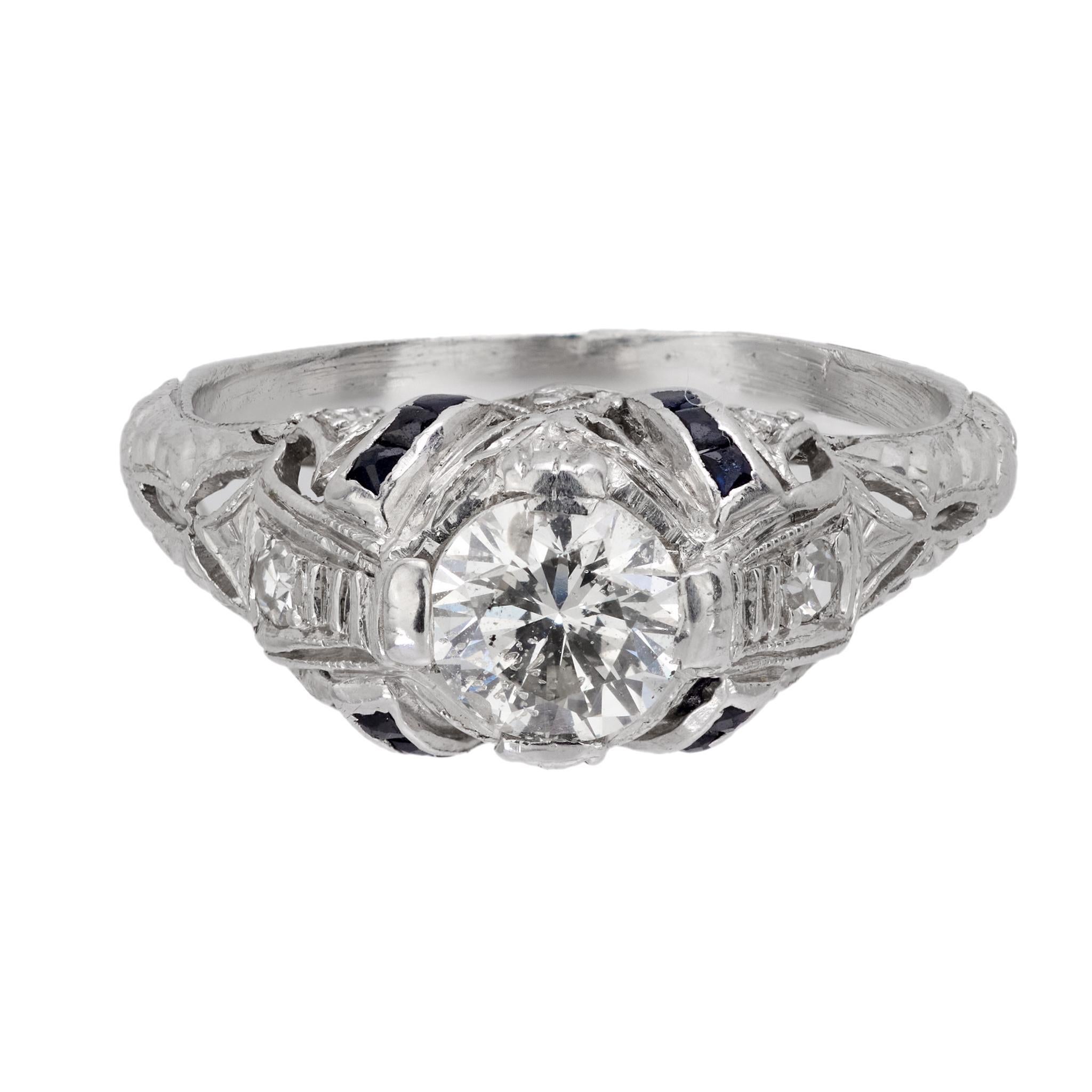 Crafted in the 1930s, this Art Deco engagement ring highlights a round brilliant cut diamond weighing approximately .50 carats, graded G color and I1 clarity. It is accented by two single cut diamonds and twelve calibre cut sapphires, totaling