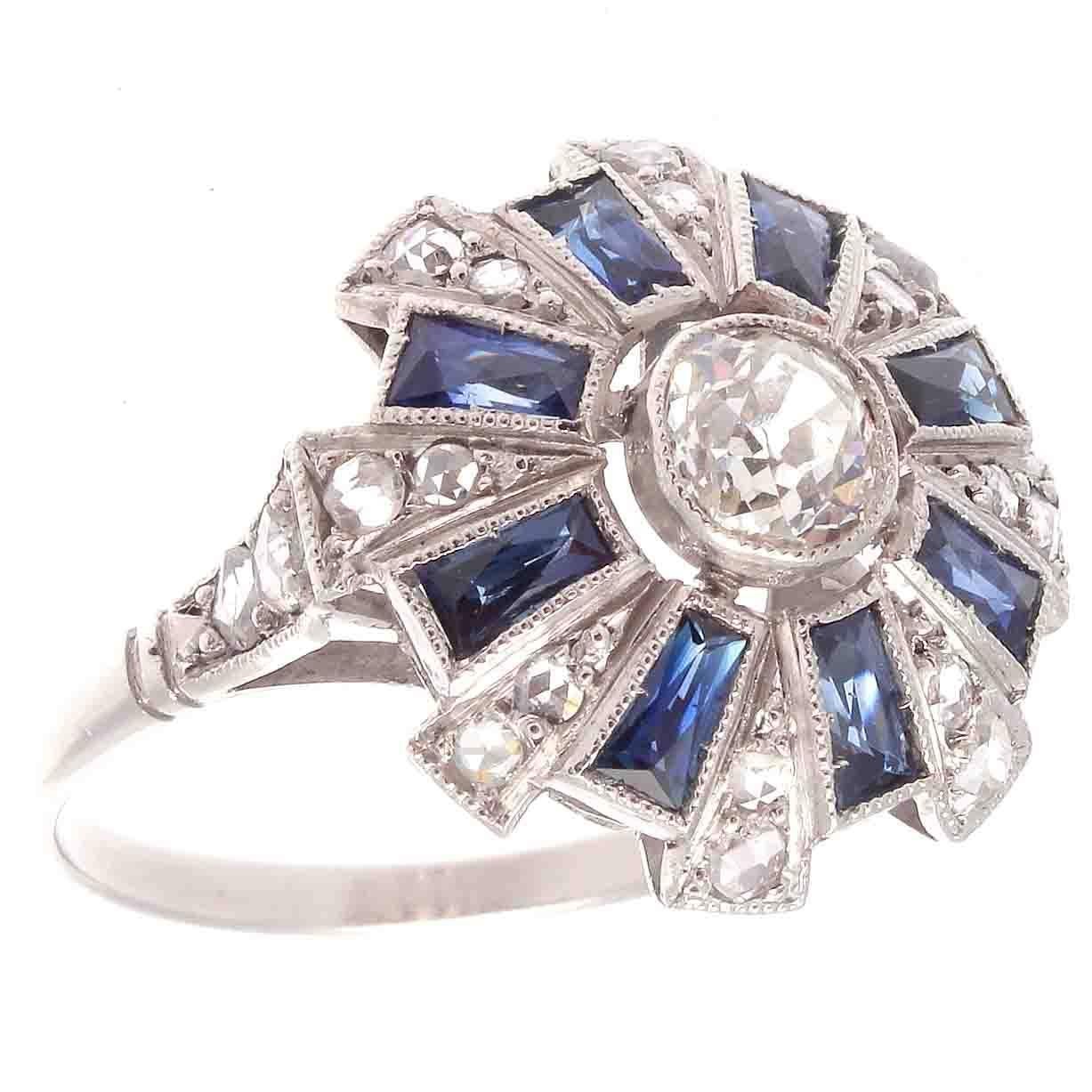 A blend of geometric shapes, key to art deco design, comes together to create one spectacular piece of jewelry. Featuring a 0.35 carat old european cut diamond that is J color, VS clarity. Accented by rays of navy blue baguette cut sapphires