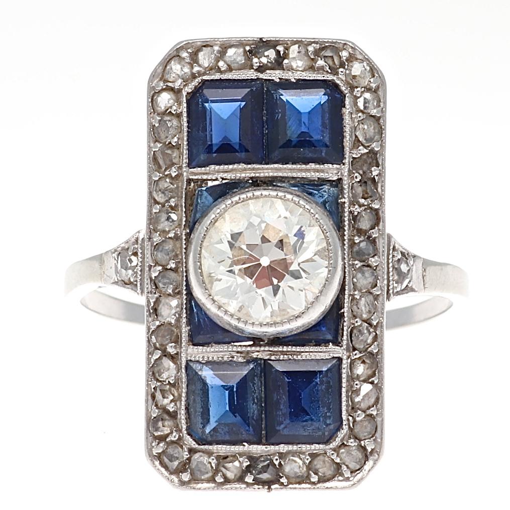 Art Deco is known for geometric shapes made so the eye can linger and appreciate it’s beauty. Used in all forms but especially in jewelry. Featuring a radiating old European cut diamond set among calibrated royal blue natural sapphires outlined in a