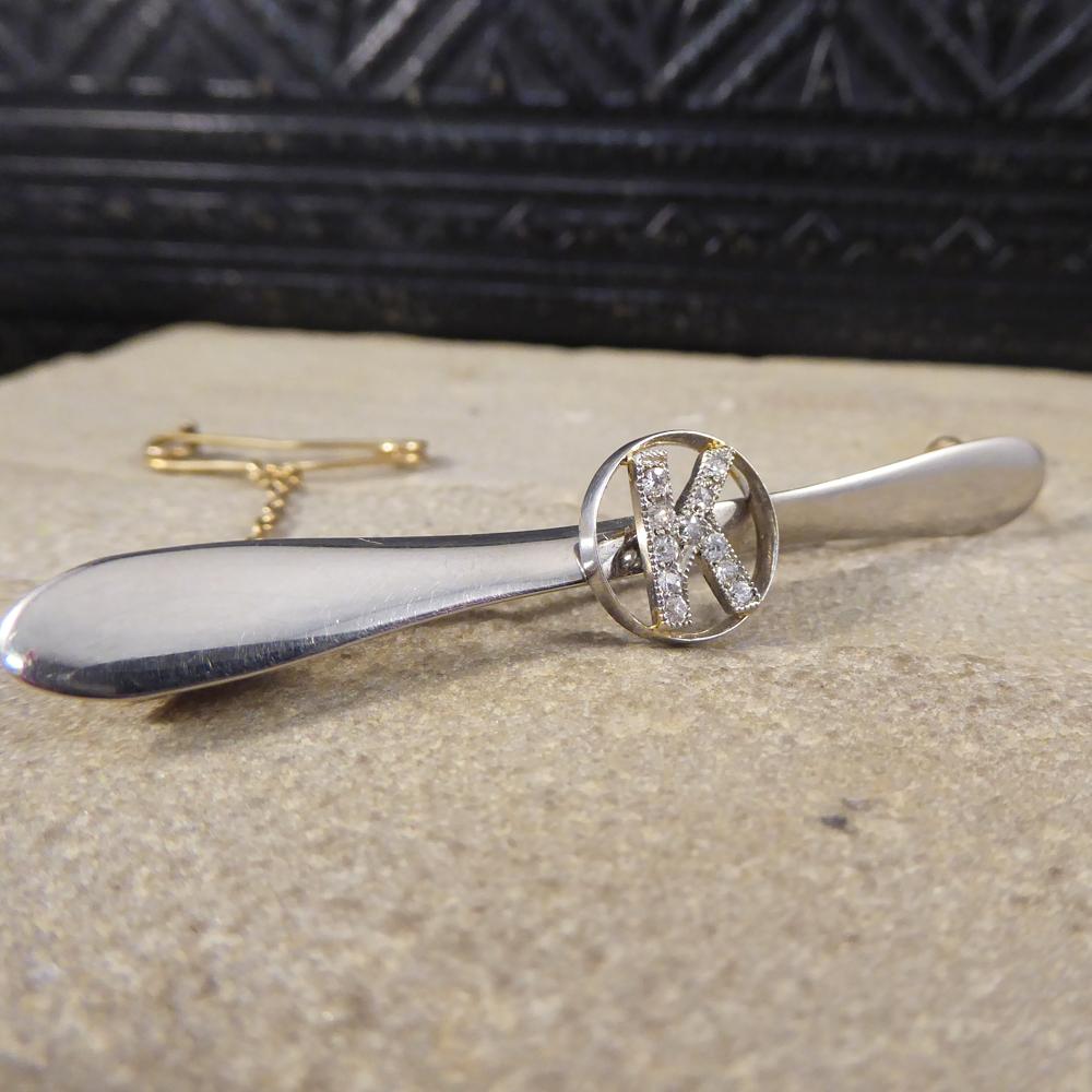 This lovely little Art Deco airplane propeller brooch is modelled in 18ct Yellow and White gold with a Yellow Gold safety chain attached. It features the initial 'K' set with Diamonds in a circle in the centre of the propeller, comes in the original