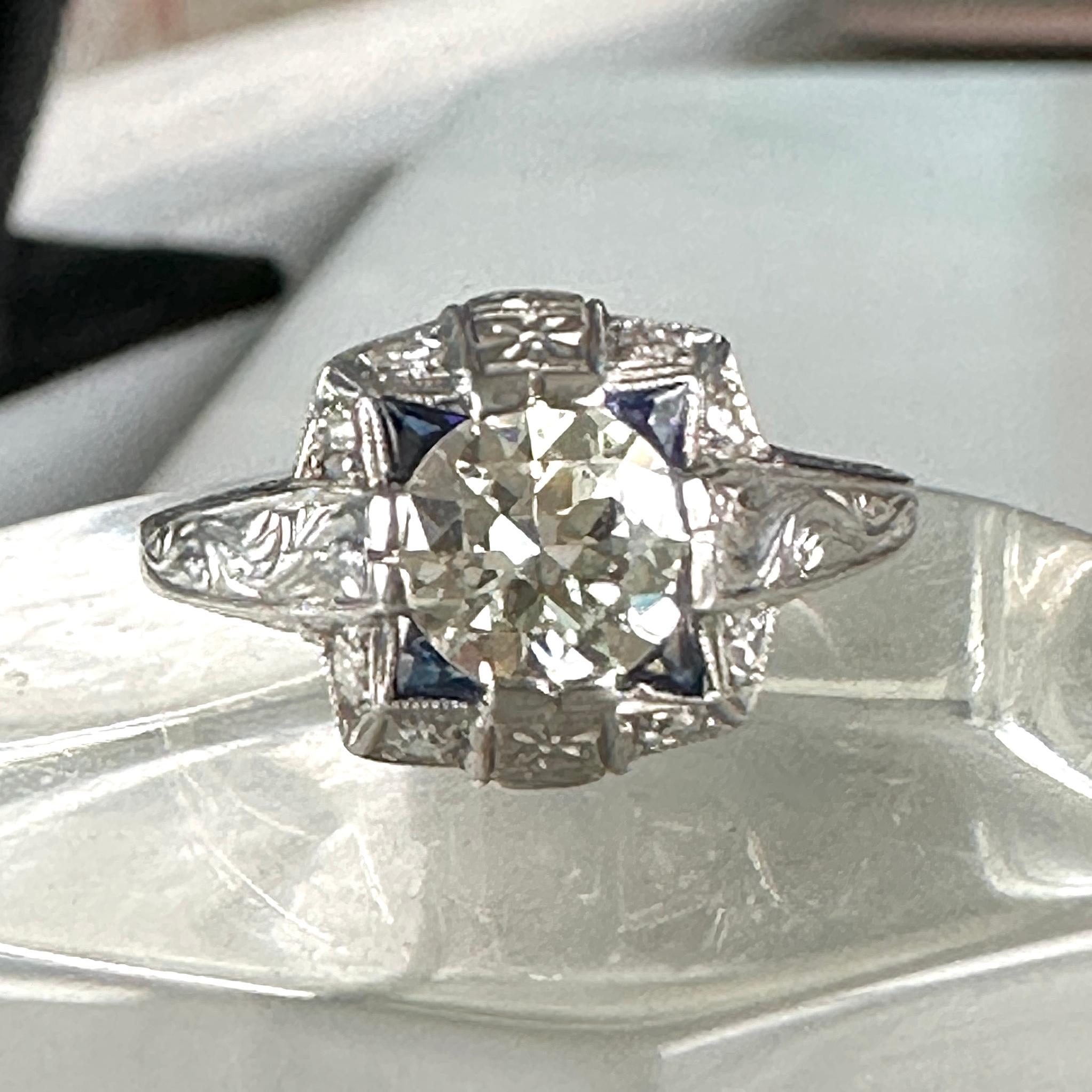 Details:
Stunning Antique Art Deco  diamond & synthetic sapphire engagement ring. The band is platinum. This is a gorgeous ring with lovely engraving around the shoulders of the band, and has engraving details surrounding the diamond. This ring is