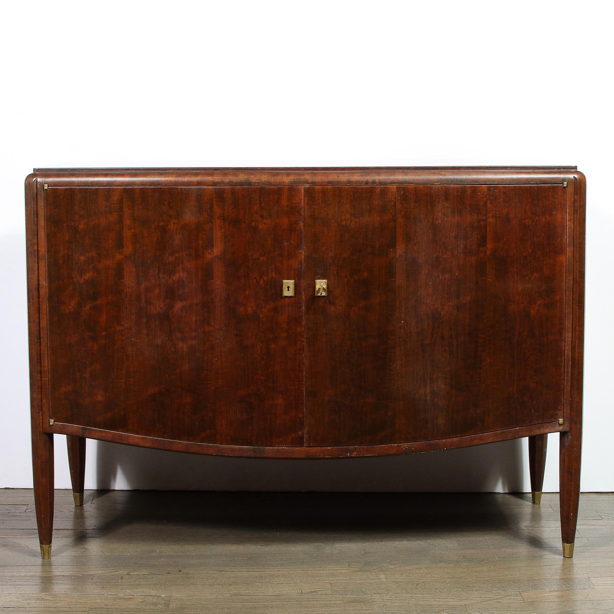 This elegant Art Deco directoire style cabinet was realized in France by the celebrated designer, Jules Leleu, circa 1940. It features a volumetric rectangular body with an undulating curved apron, as well as faceted tapered legs sitting on bronze