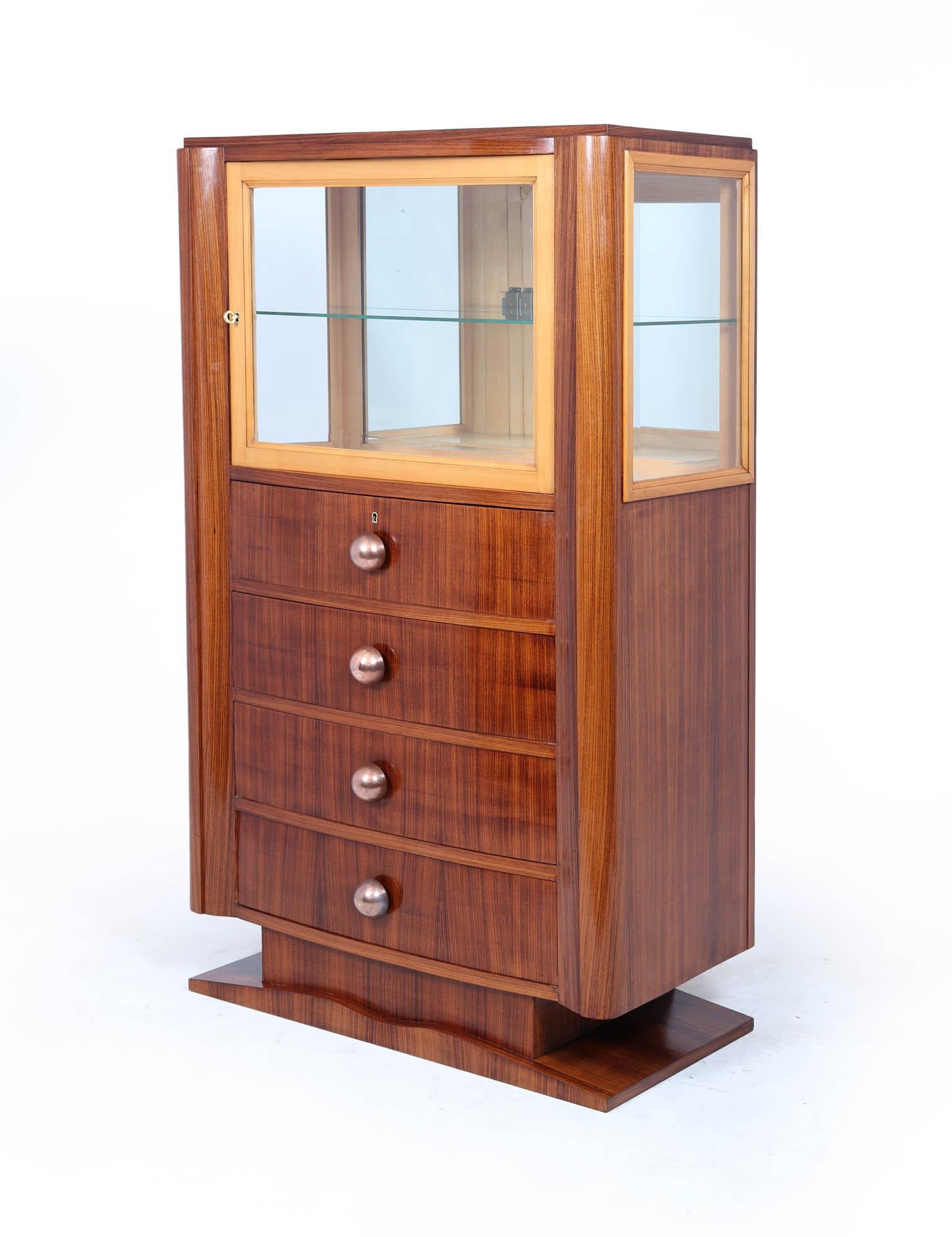 An elegant and compact Art Deco display cabinet dating to the 1930s. Crafted in richly grained Indian rosewood with a deep, warm tone and softly rounded corners, this piece offers both functionality and streamlined period charm. The upper section