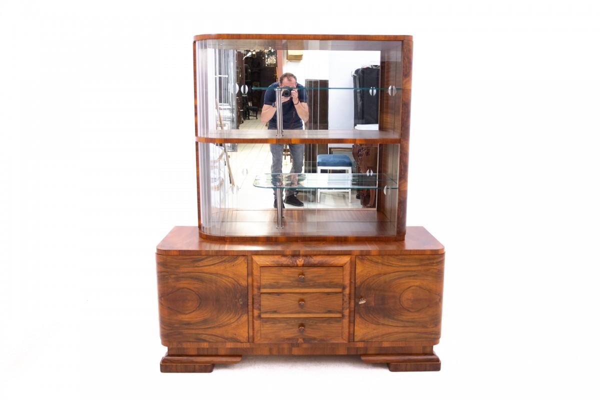 Vitrine Art Déco des années 1940, Pologne.

Un meuble à la forme géométrique caractéristique du style Art déco. La partie supérieure de la vitrine est divisée en deux parties par une étagère en bois, chacune étant dotée d'une paire de portes